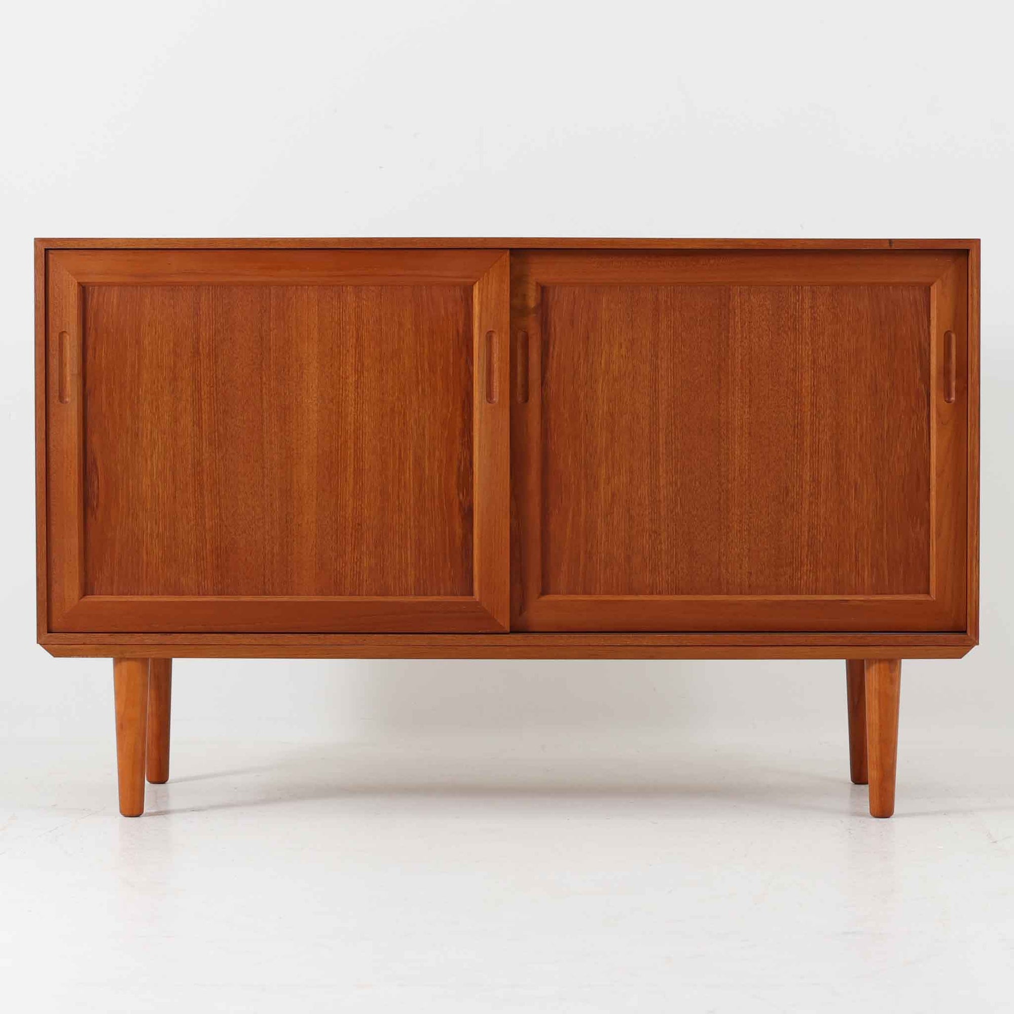 デンマーク製のこちらのローボードは、温かみあるチーク材を用いた端正な佇まいが魅力で、枠組みに厚みをもたせたスライド扉や細身のテーパー脚など、北欧ビンテージらしい上質な意匠が随所に感じられる一台です。内部は左右で棚構成が異なり、日用品から書類、メディア類まで整理しやすく、テレビボードやサイドキャビネットとしても活躍します。経年により深みを増した木肌の美しさと、シンプルながら丁寧に仕上げられた職人技が空間に落ち着きと温もりを添えるビンテージ家具です。