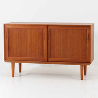 デンマーク製のこちらのローボードは、温かみあるチーク材を用いた端正な佇まいが魅力で、枠組みに厚みをもたせたスライド扉や細身のテーパー脚など、北欧ビンテージらしい上質な意匠が随所に感じられる一台です。内部は左右で棚構成が異なり、日用品から書類、メディア類まで整理しやすく、テレビボードやサイドキャビネットとしても活躍します。経年により深みを増した木肌の美しさと、シンプルながら丁寧に仕上げられた職人技が空間に落ち着きと温もりを添えるビンテージ家具です。