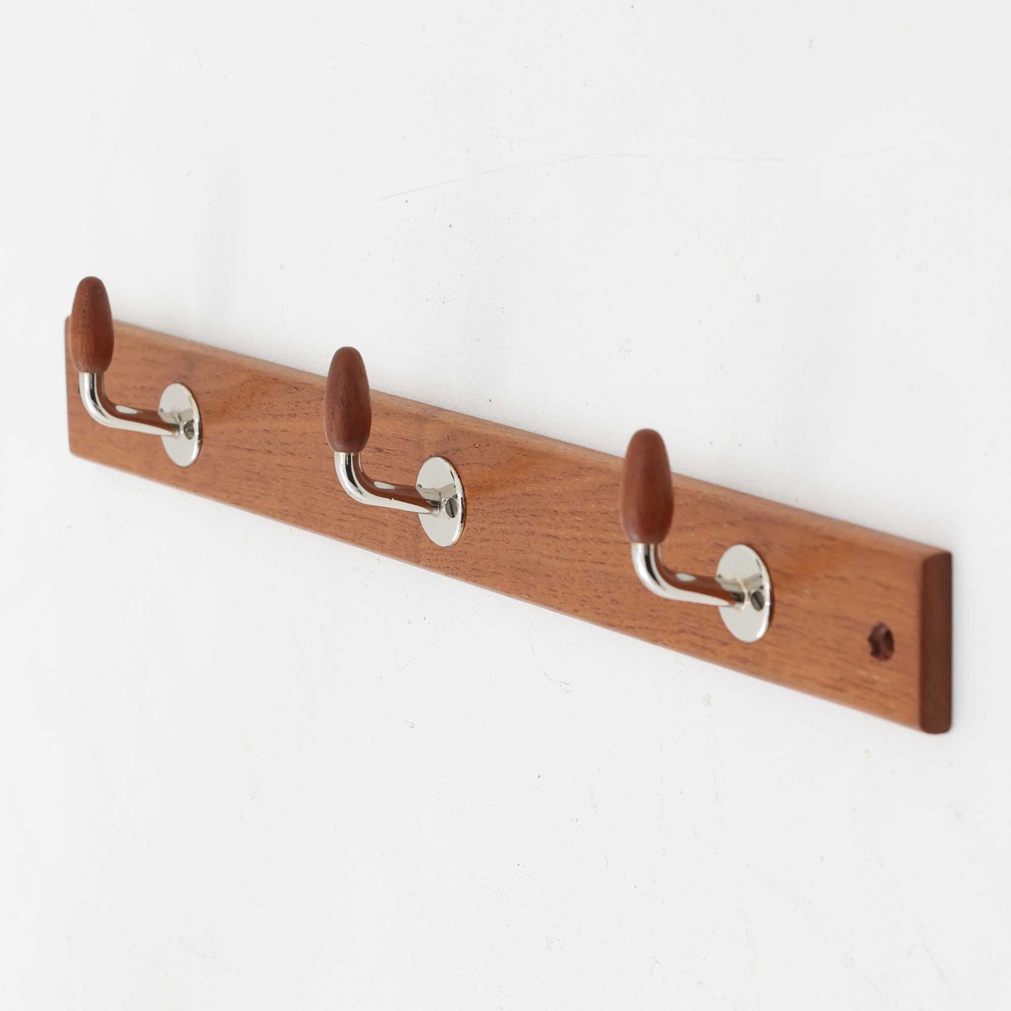 チーク材の温かみあるベースにメタル製の3連フックを組み合わせたデンマーク製のウォールハンガーです。丸みのある木製キャップ付きのフックはコートやバッグを掛けても傷つきにくく、機能性とデザイン性を両立した北欧ビンテージらしいディテールが魅力です。玄関や寝室、ワークスペースなど壁面を活用した収納に便利で、単体での使用はもちろん複数並べて使用しても美しく空間に溶け込みます。ミニマルなデザインでインテリアを選ばず永くお使いいただけるアイテムです。