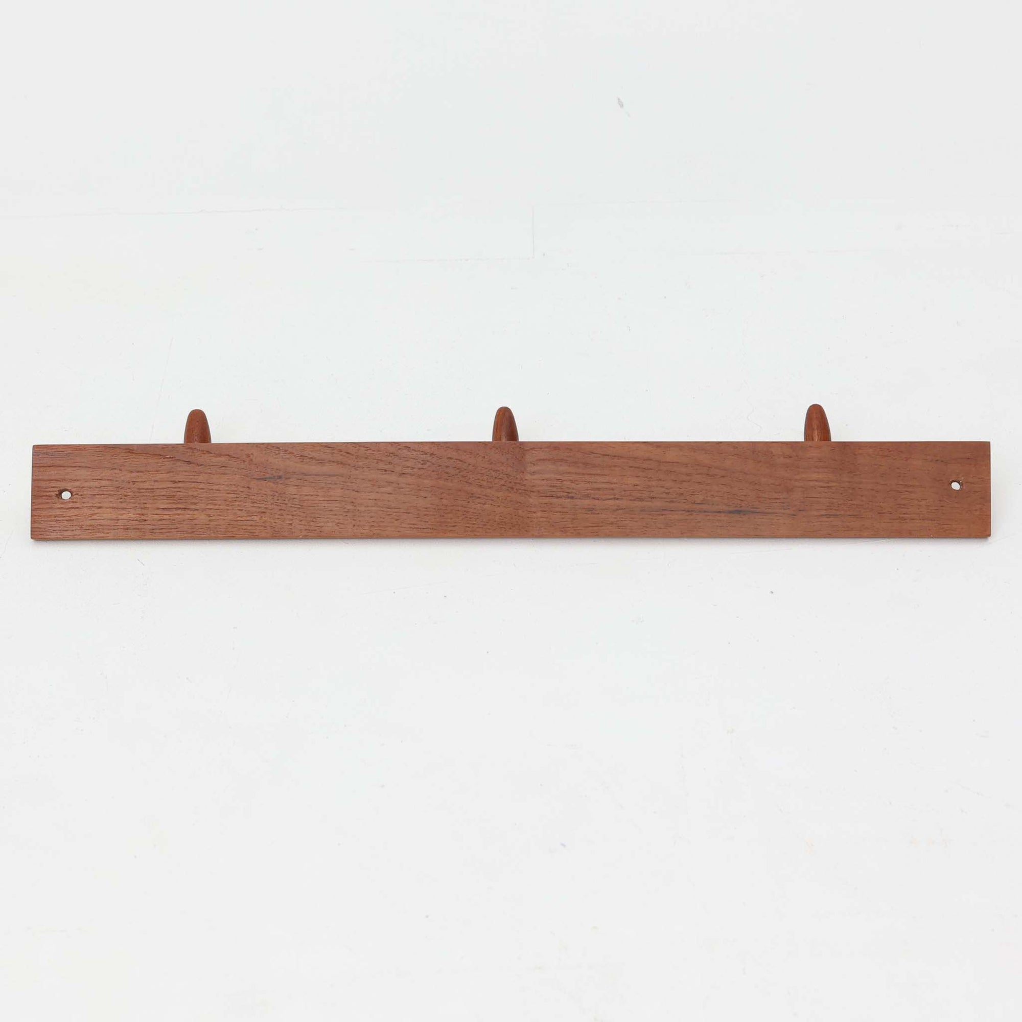 チーク材の温かみあるベースにメタル製の3連フックを組み合わせたデンマーク製のウォールハンガーです。丸みのある木製キャップ付きのフックはコートやバッグを掛けても傷つきにくく、機能性とデザイン性を両立した北欧ビンテージらしいディテールが魅力です。玄関や寝室、ワークスペースなど壁面を活用した収納に便利で、単体での使用はもちろん複数並べて使用しても美しく空間に溶け込みます。ミニマルなデザインでインテリアを選ばず永くお使いいただけるアイテムです。
