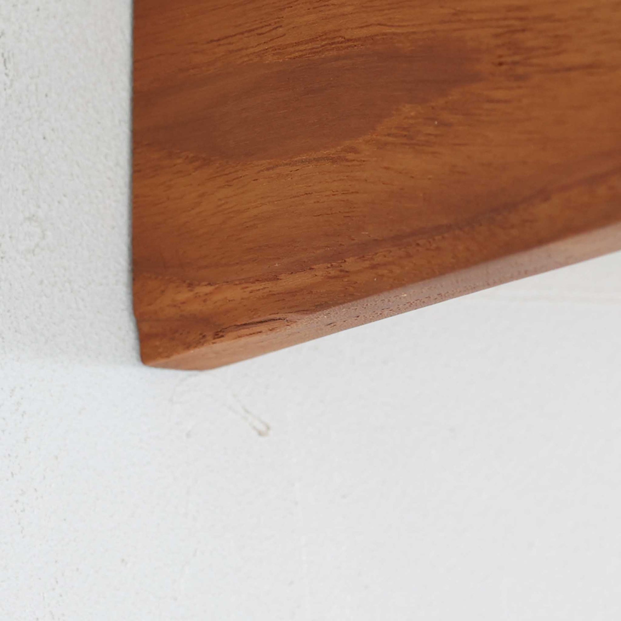 チーク材を用いたこちらのウォールシェルフは、直線的な棚板に両端の立ち上がりを設けた端正なフォルムが印象的な北欧ビンテージ家具です。前面には掘り込み式の取っ手を備えた引き出しが組み込まれており、見た目の軽やかさを保ちながら、実用的な収納力も確保しています。壁面を有効活用できる構造のため、デスク上やベッドサイド、玄関周りの小物収納としても取り入れやすく、側板は縁に向かって面取りが施され、厚みの変化によって立体感と柔らかな印象を与えています。経年により深みを増したチーク材の木目と丁寧な作りが、空間に静かな存在感を添える一台です。