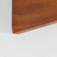 チーク材を用いたこちらのウォールシェルフは、直線的な棚板に両端の立ち上がりを設けた端正なフォルムが印象的な北欧ビンテージ家具です。前面には掘り込み式の取っ手を備えた引き出しが組み込まれており、見た目の軽やかさを保ちながら、実用的な収納力も確保しています。壁面を有効活用できる構造のため、デスク上やベッドサイド、玄関周りの小物収納としても取り入れやすく、側板は縁に向かって面取りが施され、厚みの変化によって立体感と柔らかな印象を与えています。経年により深みを増したチーク材の木目と丁寧な作りが、空間に静かな存在感を添える一台です。