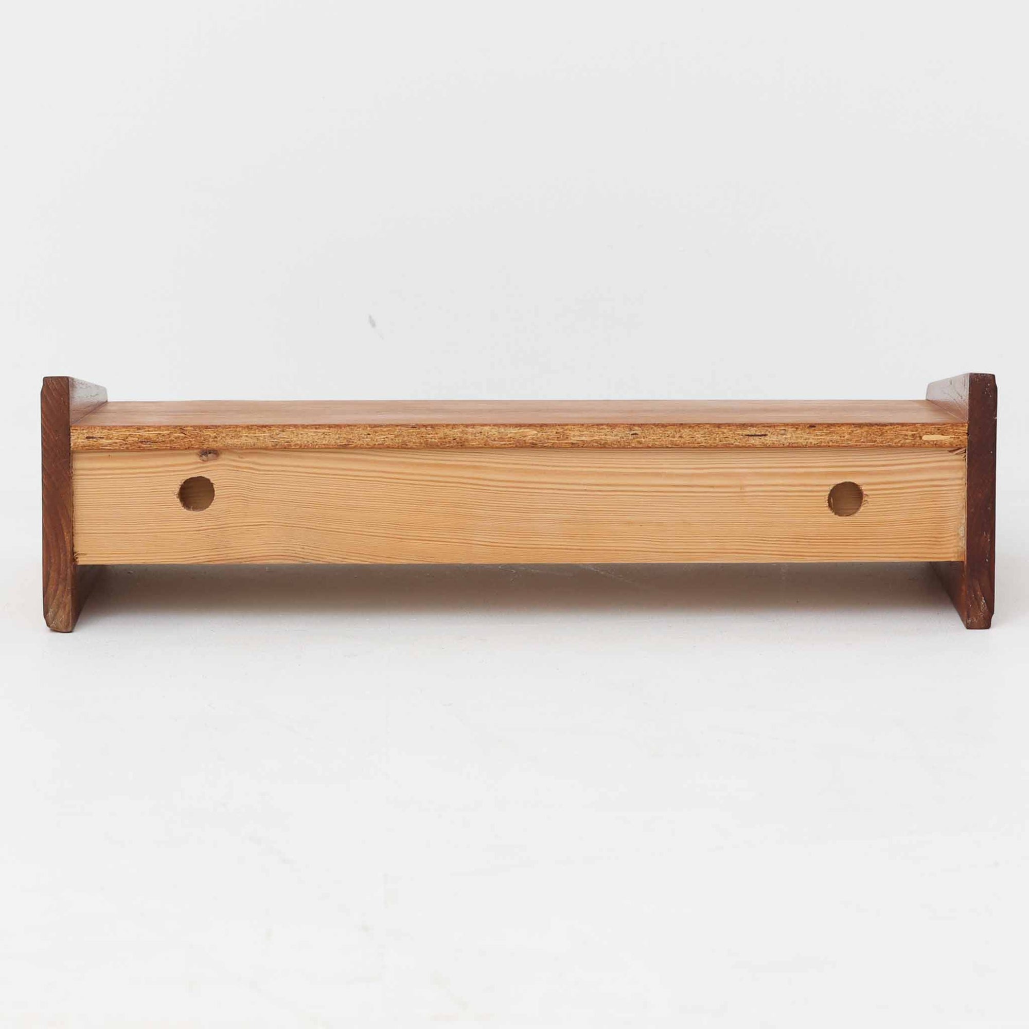 チーク材を用いたこちらのウォールシェルフは、直線的な棚板に両端の立ち上がりを設けた端正なフォルムが印象的な北欧ビンテージ家具です。前面には掘り込み式の取っ手を備えた引き出しが組み込まれており、見た目の軽やかさを保ちながら、実用的な収納力も確保しています。壁面を有効活用できる構造のため、デスク上やベッドサイド、玄関周りの小物収納としても取り入れやすく、側板は縁に向かって面取りが施され、厚みの変化によって立体感と柔らかな印象を与えています。経年により深みを増したチーク材の木目と丁寧な作りが、空間に静かな存在感を添える一台です。