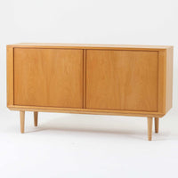 Poul Hundevadがデザインし、Hundevad & Coより製作された蛇腹仕様のサイドボードです。オーク材の穏やかで上品な木目を活かした外観に、横方向へ滑らかに開閉する蛇腹扉を組み合わせた、機能美あふれる一台。扉の開閉時に前後のスペースを取らない構造は、動線を妨げず実用性にも優れています。内部は棚板構成で収納力が高く、食器や書類、リビング周りの小物まで幅広く対応。細身の脚部が全体を軽やかに引き締め、経年によって深みを増した素材感が北欧ビンテージならではの静かな存在感を空間にもたらします。