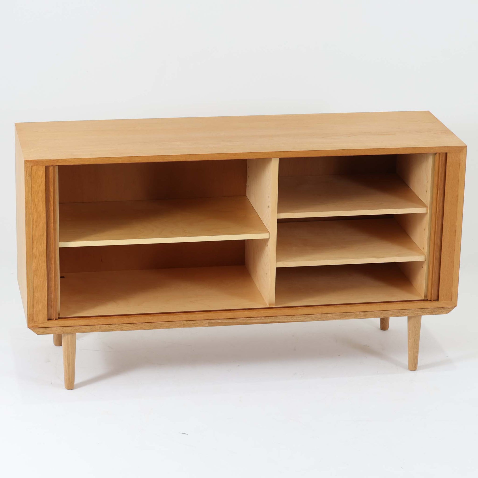 Poul Hundevadがデザインし、Hundevad &amp; Coより製作された蛇腹仕様のサイドボードです。オーク材の穏やかで上品な木目を活かした外観に、横方向へ滑らかに開閉する蛇腹扉を組み合わせた、機能美あふれる一台。扉の開閉時に前後のスペースを取らない構造は、動線を妨げず実用性にも優れています。内部は棚板構成で収納力が高く、食器や書類、リビング周りの小物まで幅広く対応。細身の脚部が全体を軽やかに引き締め、経年によって深みを増した素材感が北欧ビンテージならではの静かな存在感を空間にもたらします。