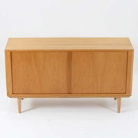 Poul Hundevadがデザインし、Hundevad & Coより製作された蛇腹仕様のサイドボードです。オーク材の穏やかで上品な木目を活かした外観に、横方向へ滑らかに開閉する蛇腹扉を組み合わせた、機能美あふれる一台。扉の開閉時に前後のスペースを取らない構造は、動線を妨げず実用性にも優れています。内部は棚板構成で収納力が高く、食器や書類、リビング周りの小物まで幅広く対応。細身の脚部が全体を軽やかに引き締め、経年によって深みを増した素材感が北欧ビンテージならではの静かな存在感を空間にもたらします。