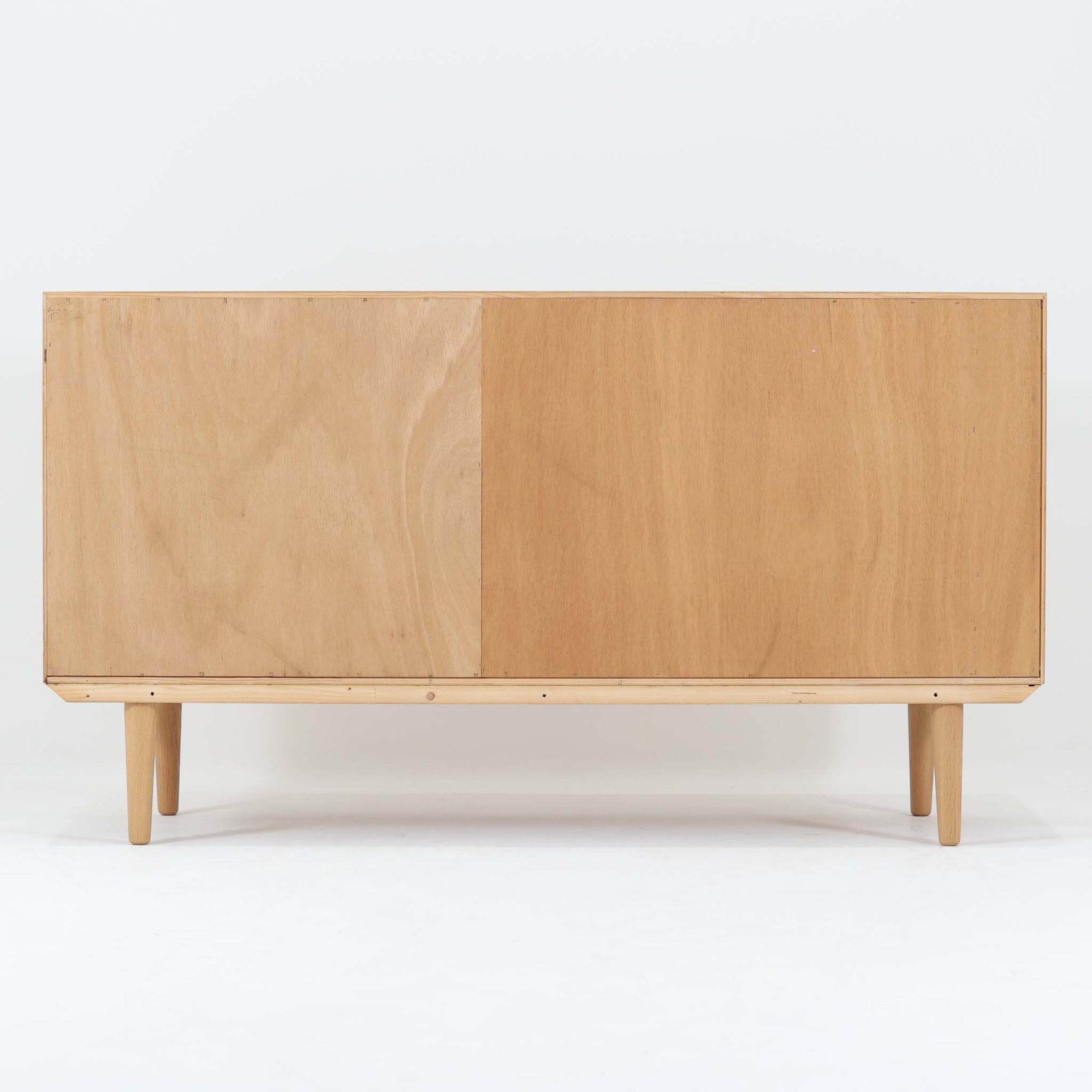 Poul Hundevadがデザインし、Hundevad &amp; Coより製作された蛇腹仕様のサイドボードです。オーク材の穏やかで上品な木目を活かした外観に、横方向へ滑らかに開閉する蛇腹扉を組み合わせた、機能美あふれる一台。扉の開閉時に前後のスペースを取らない構造は、動線を妨げず実用性にも優れています。内部は棚板構成で収納力が高く、食器や書類、リビング周りの小物まで幅広く対応。細身の脚部が全体を軽やかに引き締め、経年によって深みを増した素材感が北欧ビンテージならではの静かな存在感を空間にもたらします。