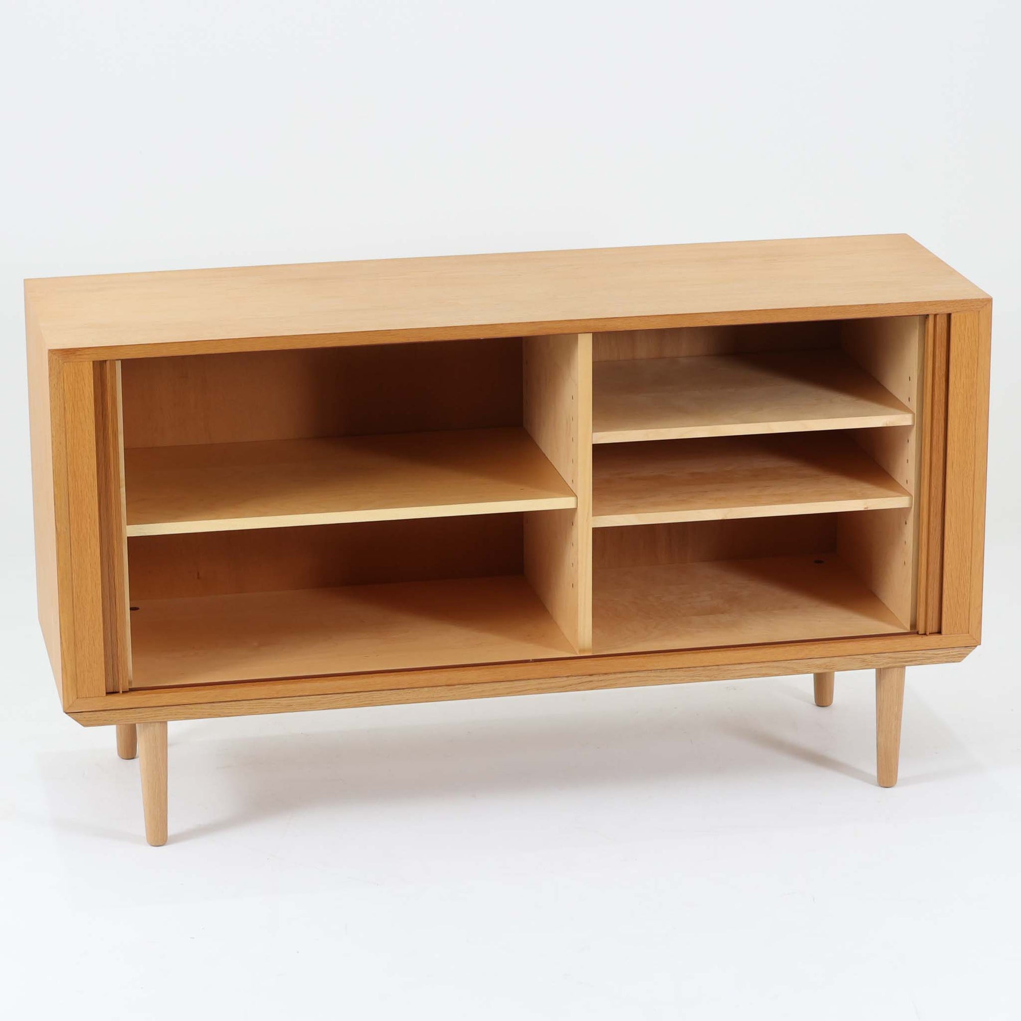 Poul Hundevadがデザインし、Hundevad &amp; Coより製作された蛇腹仕様のサイドボードです。オーク材の穏やかで上品な木目を活かした外観に、横方向へ滑らかに開閉する蛇腹扉を組み合わせた、機能美あふれる一台。扉の開閉時に前後のスペースを取らない構造は、動線を妨げず実用性にも優れています。内部は棚板構成で収納力が高く、食器や書類、リビング周りの小物まで幅広く対応。細身の脚部が全体を軽やかに引き締め、経年によって深みを増した素材感が北欧ビンテージならではの静かな存在感を空間にもたらします。