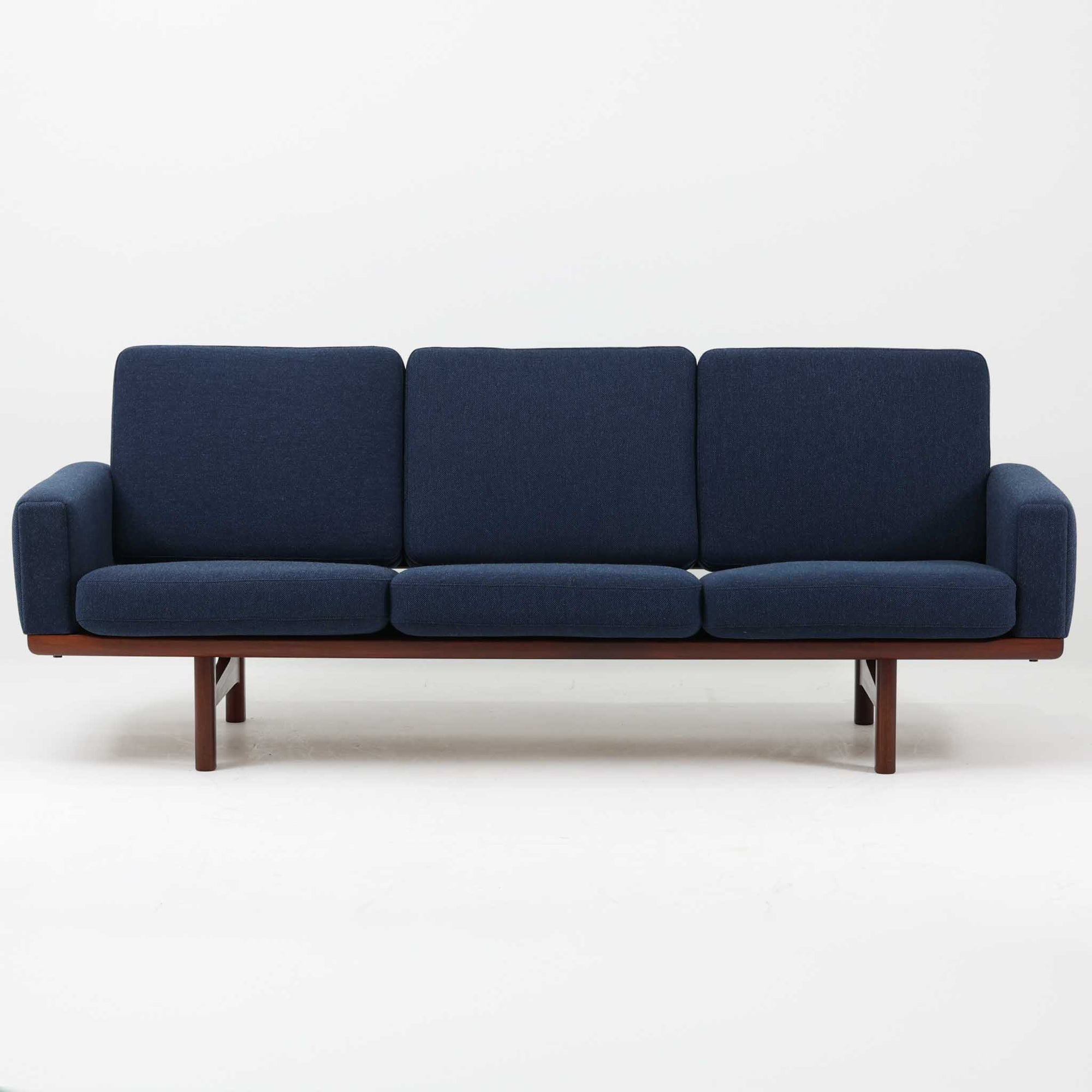 こちらは、ウェグナーデザインの人気モデル、GE236の3人掛けソファです。後ろ姿が非常に美しいため、あえて壁に寄せず背面を見せる配置もおすすめです。クッション内部にはスプリングが内蔵されており、座り心地も良好です。さらに、こちらは現地でも希少なアフロモシア材（通称アフリカンチーク）が使用された特別なモデルです。GE236のチーク材仕様として一般的に認識されているのは、このアフロモシア材が使用されたモデルを指します。GETAMA社の刻印も確認できます。