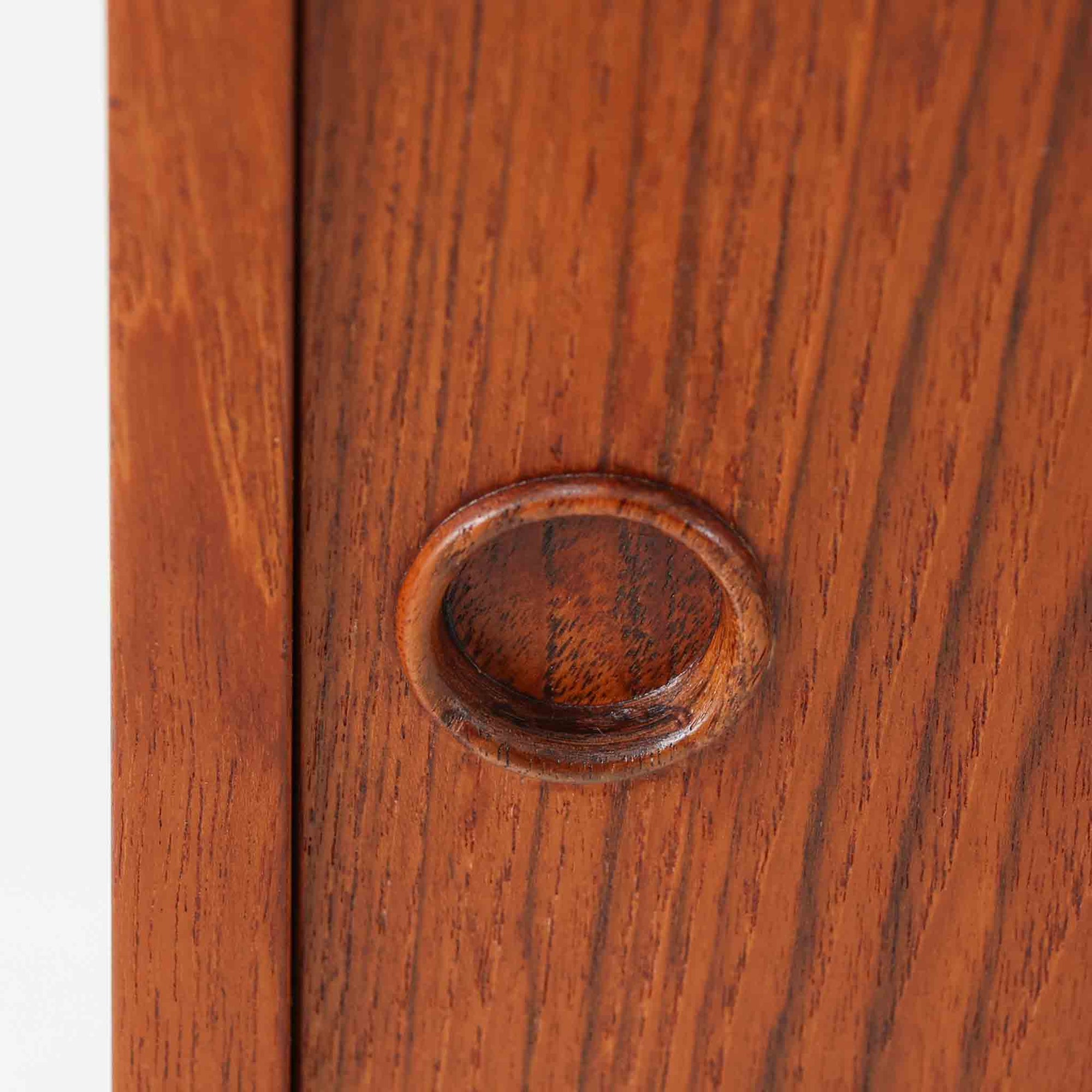 デンマーク製ローボードです。チーク材ならではの赤みを帯びた美しい木目が前面にあらわれ、引き戸には掘り込み式の丸い取っ手を配したミニマルな意匠が北欧らしい静かな存在感を放ちます。幅80cmの小ぶりなサイズ感で、リビングのテレビ台としてはもちろん、書斎やベッドルームでの収納家具としても取り入れやすく、内部には棚板を備え実用性も十分です。経年によって深みを増した木肌の表情と丁寧なつくりが、ビンテージならではの温もりを空間に添えてくれる一台です。