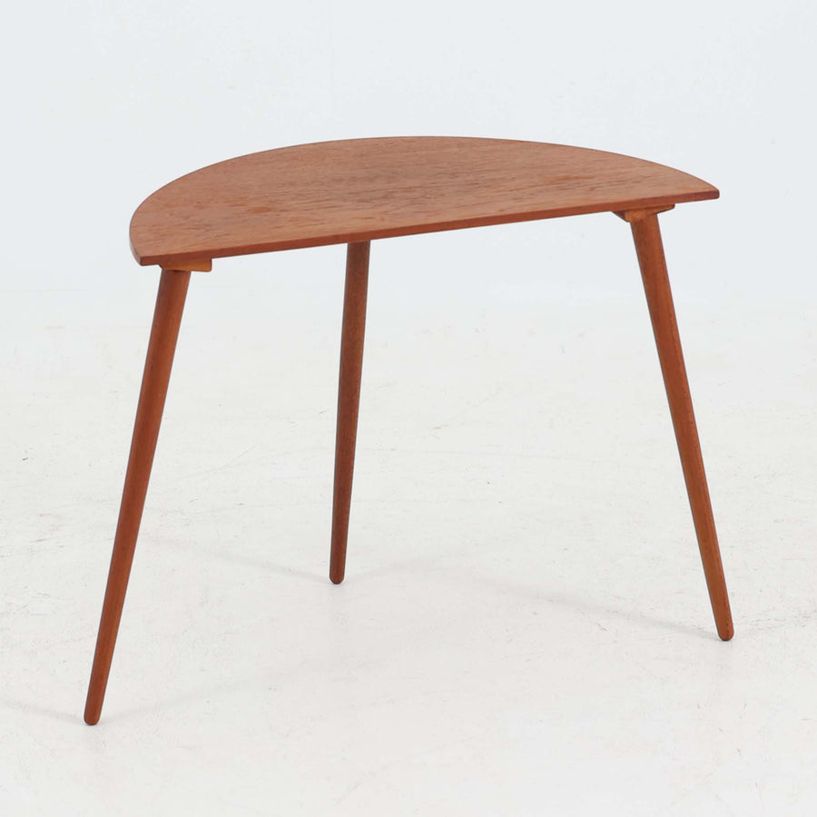 デンマーク製サイドテーブルです。チーク材を使用し、滑らかな半円形の天板とすらりと伸びた3本の円錐脚が軽やかな印象を与えます。北欧デザインらしいミニマルな造形ながら、チーク材の温かみと艶が経年変化によって美しく際立っています。ソファ横やベッドサイドなど、限られたスペースにも馴染むサイズ感で、花瓶やランプを置く飾り台としてもおすすめの一台です。