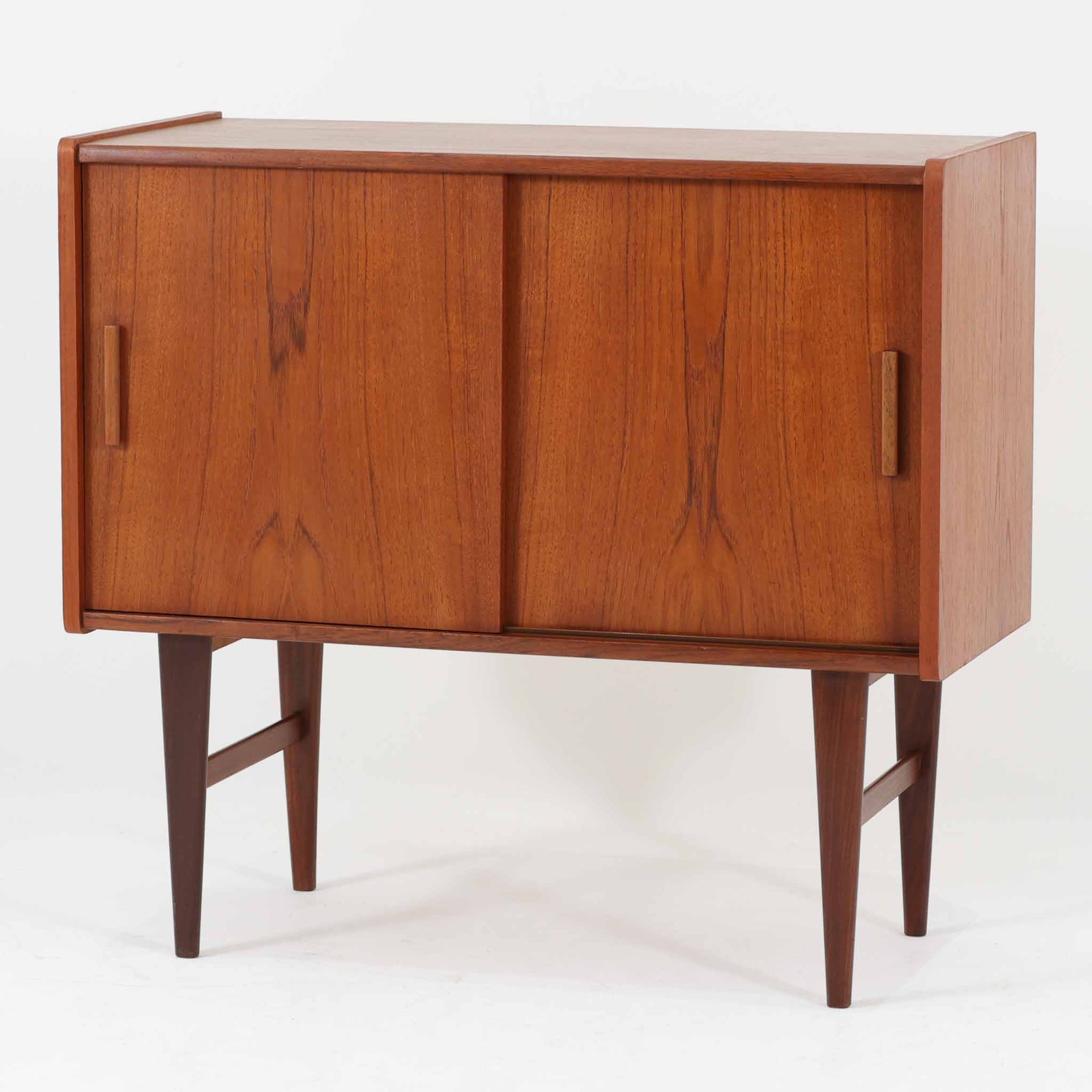 北欧ビンテージらしい端正な佇まいが魅力の小ぶりなボードです。深みのある色合いが美しいチーク材が用いられ、木目の表情と経年変化による艶感が空間に落ち着きを与えます。引き戸仕様の扉は前後にスペースを取らず、限られた空間でも扱いやすい構造です。内部には棚板を備え、食器や書類、小物類まですっきりと収納可能。幅80cmのコンパクトなサイズ感は、リビングのサブ収納や玄関、書斎など多用途に活躍し、北欧家具ならではの実用性と素材の良さを感じさせる一台です。