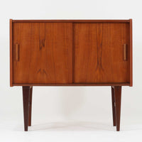 北欧ビンテージらしい端正な佇まいが魅力の小ぶりなボードです。深みのある色合いが美しいチーク材が用いられ、木目の表情と経年変化による艶感が空間に落ち着きを与えます。引き戸仕様の扉は前後にスペースを取らず、限られた空間でも扱いやすい構造です。内部には棚板を備え、食器や書類、小物類まですっきりと収納可能。幅80cmのコンパクトなサイズ感は、リビングのサブ収納や玄関、書斎など多用途に活躍し、北欧家具ならではの実用性と素材の良さを感じさせる一台です。