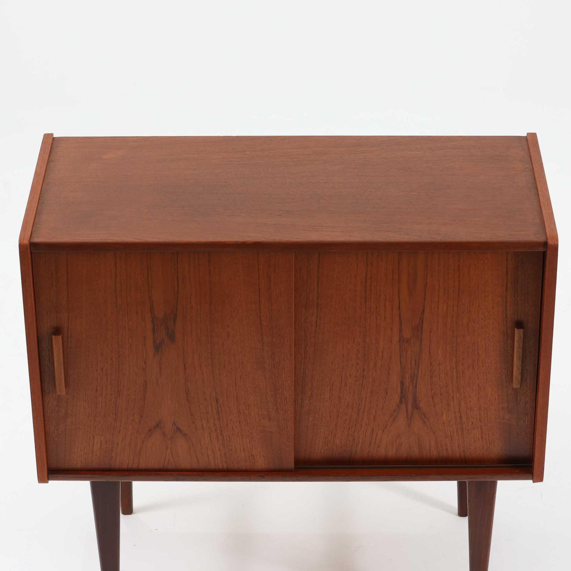 北欧ビンテージらしい端正な佇まいが魅力の小ぶりなボードです。深みのある色合いが美しいチーク材が用いられ、木目の表情と経年変化による艶感が空間に落ち着きを与えます。引き戸仕様の扉は前後にスペースを取らず、限られた空間でも扱いやすい構造です。内部には棚板を備え、食器や書類、小物類まですっきりと収納可能。幅80cmのコンパクトなサイズ感は、リビングのサブ収納や玄関、書斎など多用途に活躍し、北欧家具ならではの実用性と素材の良さを感じさせる一台です。