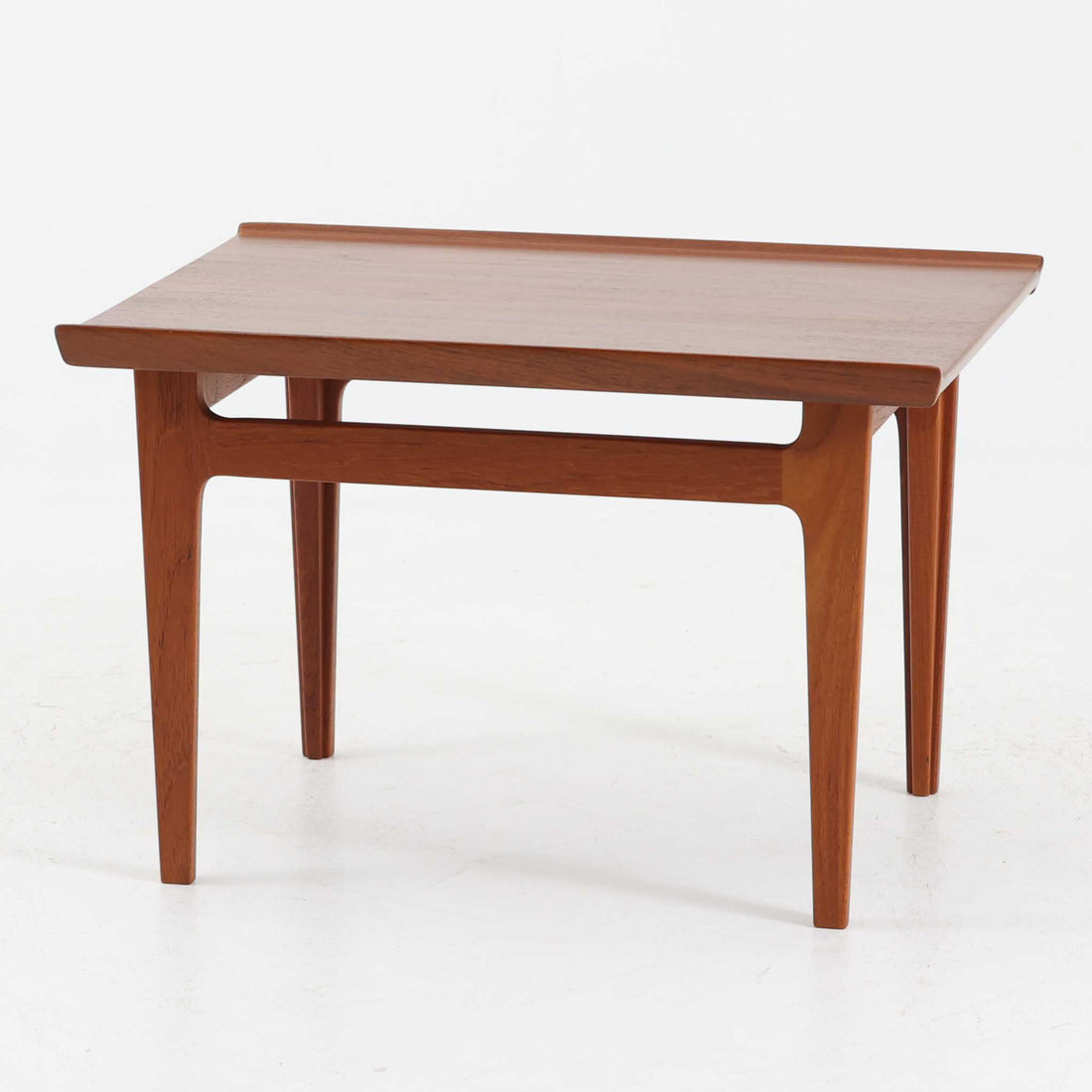 デンマークの巨匠フィン・ユールによるデザイン、France & Son社製のサイドテーブル「FD635」です。ロゴより1957～1960年代前半に製造されたと推測される本品は、チーク無垢材を贅沢に使用し、滑らかな脚部の曲線と柔らかなエッジラインが見事に調和した美しいデザインが魅力です。天板の縁にはわずかな立ち上がりが設けられ、機能性と造形美を兼ね備えた構造となっています。彫刻的ともいえる有機的なフォルムはフィン・ユールの真骨頂であり、リビングやベッドサイドで北欧家具の上質な存在感を引き立てる逸品です。