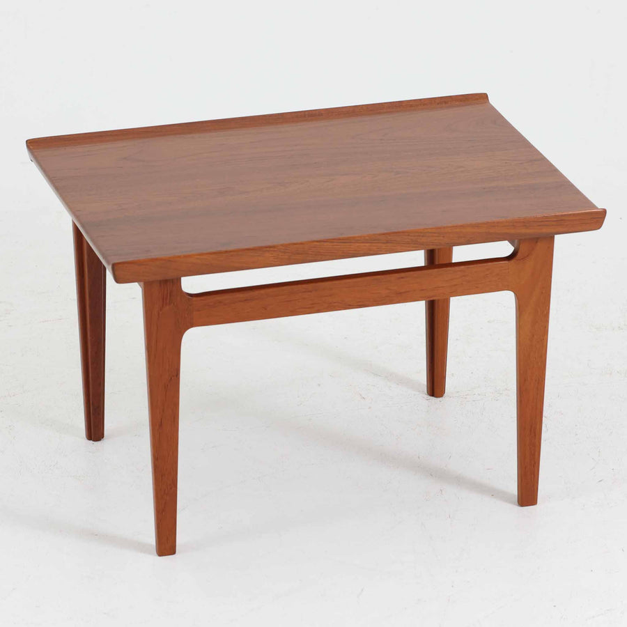 デンマークの巨匠フィン・ユールによるデザイン、France & Son社製のサイドテーブル「FD635」です。ロゴより1957～1960年代前半に製造されたと推測される本品は、チーク無垢材を贅沢に使用し、滑らかな脚部の曲線と柔らかなエッジラインが見事に調和した美しいデザインが魅力です。天板の縁にはわずかな立ち上がりが設けられ、機能性と造形美を兼ね備えた構造となっています。彫刻的ともいえる有機的なフォルムはフィン・ユールの真骨頂であり、リビングやベッドサイドで北欧家具の上質な存在感を引き立てる逸品です。