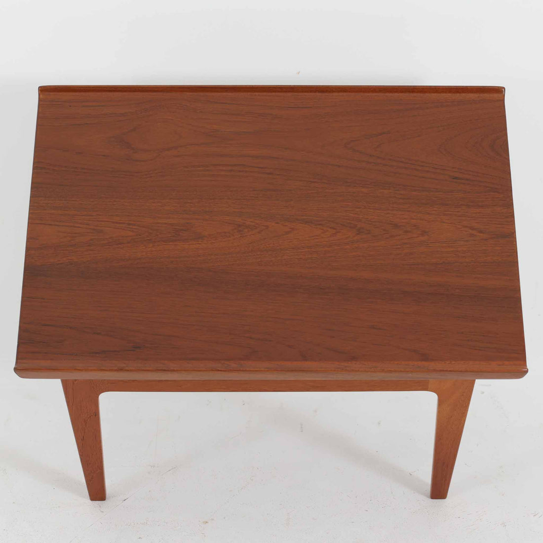 デンマークの巨匠フィン・ユールによるデザイン、France & Son社製のサイドテーブル「FD635」です。ロゴより1957～1960年代前半に製造されたと推測される本品は、チーク無垢材を贅沢に使用し、滑らかな脚部の曲線と柔らかなエッジラインが見事に調和した美しいデザインが魅力です。天板の縁にはわずかな立ち上がりが設けられ、機能性と造形美を兼ね備えた構造となっています。彫刻的ともいえる有機的なフォルムはフィン・ユールの真骨頂であり、リビングやベッドサイドで北欧家具の上質な存在感を引き立てる逸品です。