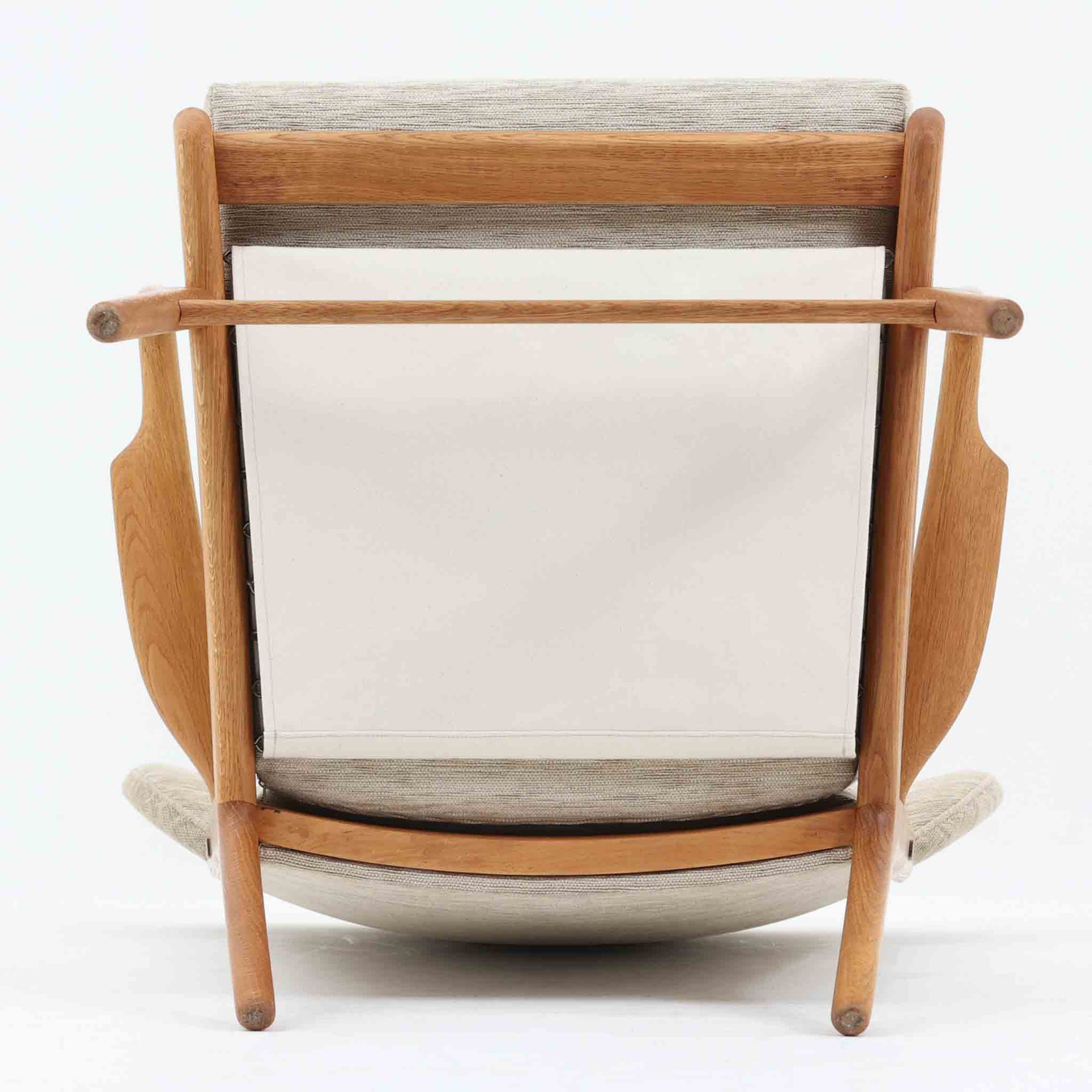 Hans J. Wegnerがデザインし、AP Stolenが製作したAP15ハイバックシングルソファです。オーク材の滑らかな木肌を活かしたフレームに、包み込むような背とヘッドレストを備えた優美なフォルムが印象的。彫刻的なアーム形状や前後に傾斜した脚部など、随所にウェグナーらしい造形美が感じられます。ホワイト系の色味が空間を明るく上品な印象に整えます。ゆったりと身体を預けられる快適な座り心地と、経年で深みを増した木部の風合いが格調ある雰囲気をもたらす北欧ビンテージの名品です。