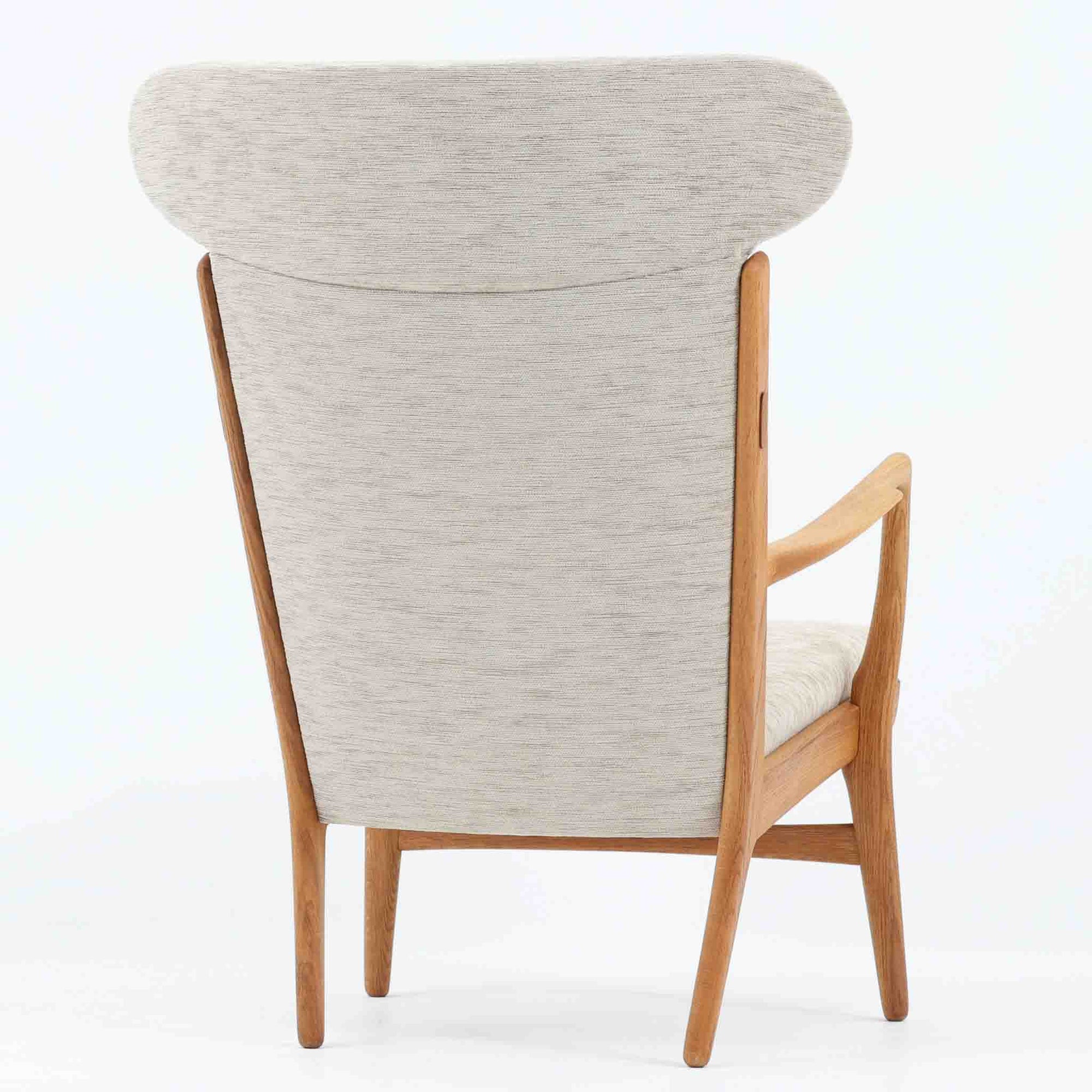 Hans J. Wegnerがデザインし、AP Stolenが製作したAP15ハイバックシングルソファです。オーク材の滑らかな木肌を活かしたフレームに、包み込むような背とヘッドレストを備えた優美なフォルムが印象的。彫刻的なアーム形状や前後に傾斜した脚部など、随所にウェグナーらしい造形美が感じられます。ホワイト系の色味が空間を明るく上品な印象に整えます。ゆったりと身体を預けられる快適な座り心地と、経年で深みを増した木部の風合いが格調ある雰囲気をもたらす北欧ビンテージの名品です。