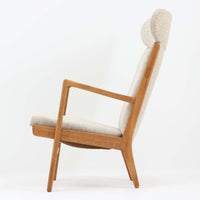 Hans J. Wegnerがデザインし、AP Stolenが製作したAP15ハイバックシングルソファです。オーク材の滑らかな木肌を活かしたフレームに、包み込むような背とヘッドレストを備えた優美なフォルムが印象的。彫刻的なアーム形状や前後に傾斜した脚部など、随所にウェグナーらしい造形美が感じられます。ホワイト系の色味が空間を明るく上品な印象に整えます。ゆったりと身体を預けられる快適な座り心地と、経年で深みを増した木部の風合いが格調ある雰囲気をもたらす北欧ビンテージの名品です。