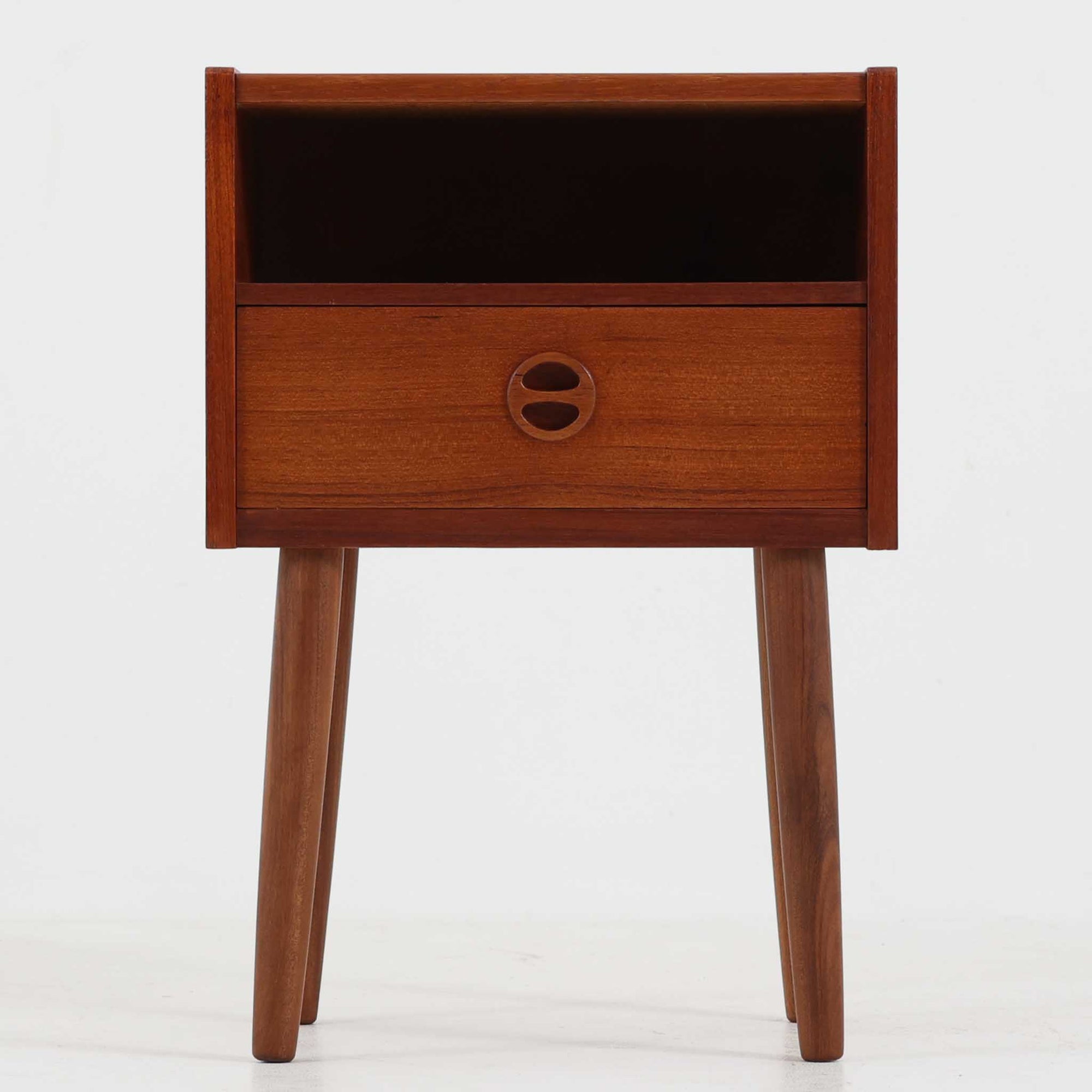 デンマーク製のサイドチェストで、温かみのあるチーク材を用いた北欧ビンテージらしい佇まいが魅力です。上段のオープンスペースは読みかけの本や小物の収納に便利で、下段の引き出しにはアイコン的な丸型取手があしらわれ、シンプルな中にも愛嬌のあるアクセントを添えています。細く伸びたテーパードレッグが軽やかな印象を与え、ベッドサイドやソファ横のサイドテーブルとしても活躍。経年変化による深い色艶が空間に上質な雰囲気をもたらすビンテージ家具です。
