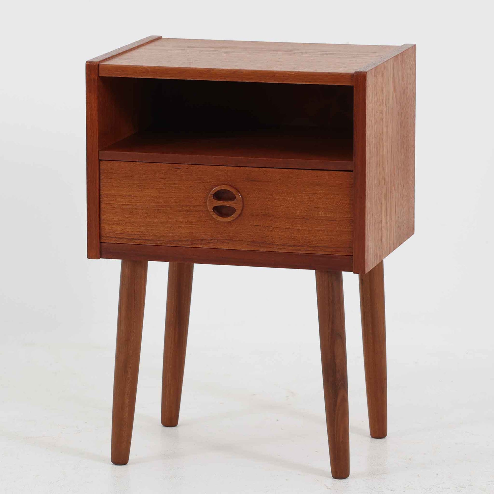 デンマーク製のサイドチェストで、温かみのあるチーク材を用いた北欧ビンテージらしい佇まいが魅力です。上段のオープンスペースは読みかけの本や小物の収納に便利で、下段の引き出しにはアイコン的な丸型取手があしらわれ、シンプルな中にも愛嬌のあるアクセントを添えています。細く伸びたテーパードレッグが軽やかな印象を与え、ベッドサイドやソファ横のサイドテーブルとしても活躍。経年変化による深い色艶が空間に上質な雰囲気をもたらすビンテージ家具です。