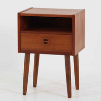 デンマーク製のサイドチェストで、温かみのあるチーク材を用いた北欧ビンテージらしい佇まいが魅力です。上段のオープンスペースは読みかけの本や小物の収納に便利で、下段の引き出しにはアイコン的な丸型取手があしらわれ、シンプルな中にも愛嬌のあるアクセントを添えています。細く伸びたテーパードレッグが軽やかな印象を与え、ベッドサイドやソファ横のサイドテーブルとしても活躍。経年変化による深い色艶が空間に上質な雰囲気をもたらすビンテージ家具です。