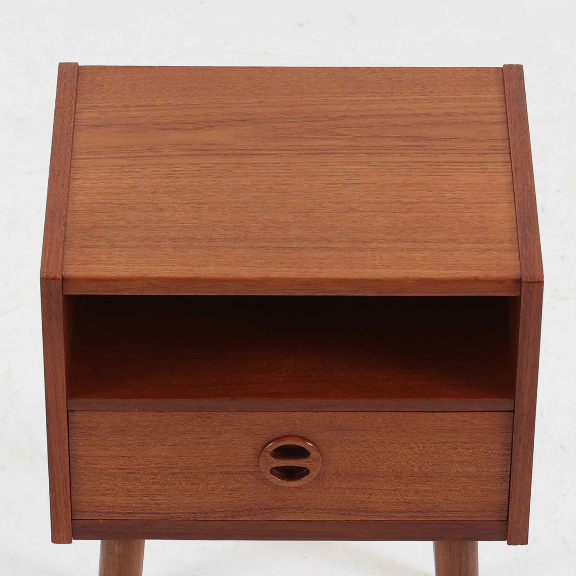 デンマーク製のサイドチェストで、温かみのあるチーク材を用いた北欧ビンテージらしい佇まいが魅力です。上段のオープンスペースは読みかけの本や小物の収納に便利で、下段の引き出しにはアイコン的な丸型取手があしらわれ、シンプルな中にも愛嬌のあるアクセントを添えています。細く伸びたテーパードレッグが軽やかな印象を与え、ベッドサイドやソファ横のサイドテーブルとしても活躍。経年変化による深い色艶が空間に上質な雰囲気をもたらすビンテージ家具です。