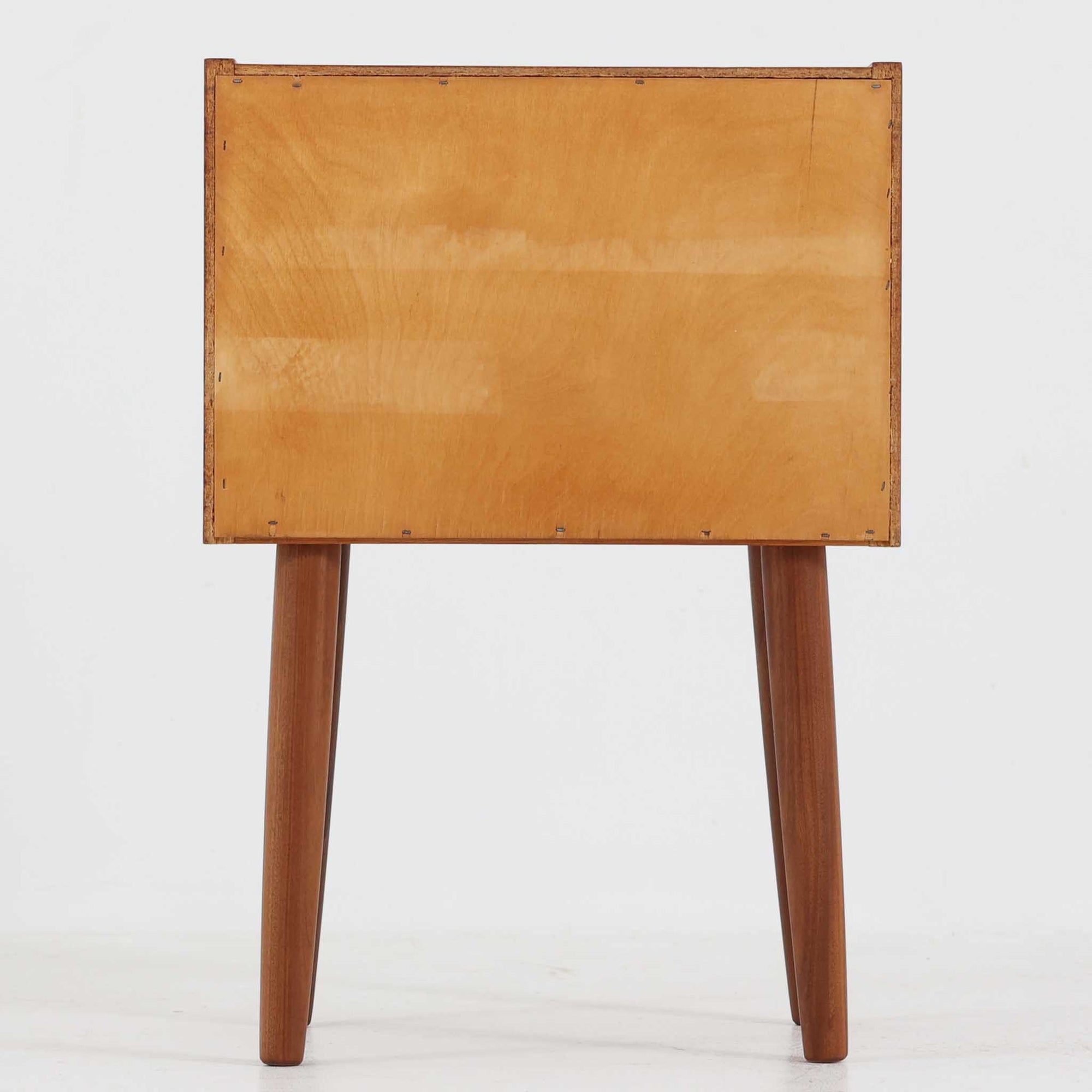 デンマーク製のサイドチェストで、温かみのあるチーク材を用いた北欧ビンテージらしい佇まいが魅力です。上段のオープンスペースは読みかけの本や小物の収納に便利で、下段の引き出しにはアイコン的な丸型取手があしらわれ、シンプルな中にも愛嬌のあるアクセントを添えています。細く伸びたテーパードレッグが軽やかな印象を与え、ベッドサイドやソファ横のサイドテーブルとしても活躍。経年変化による深い色艶が空間に上質な雰囲気をもたらすビンテージ家具です。