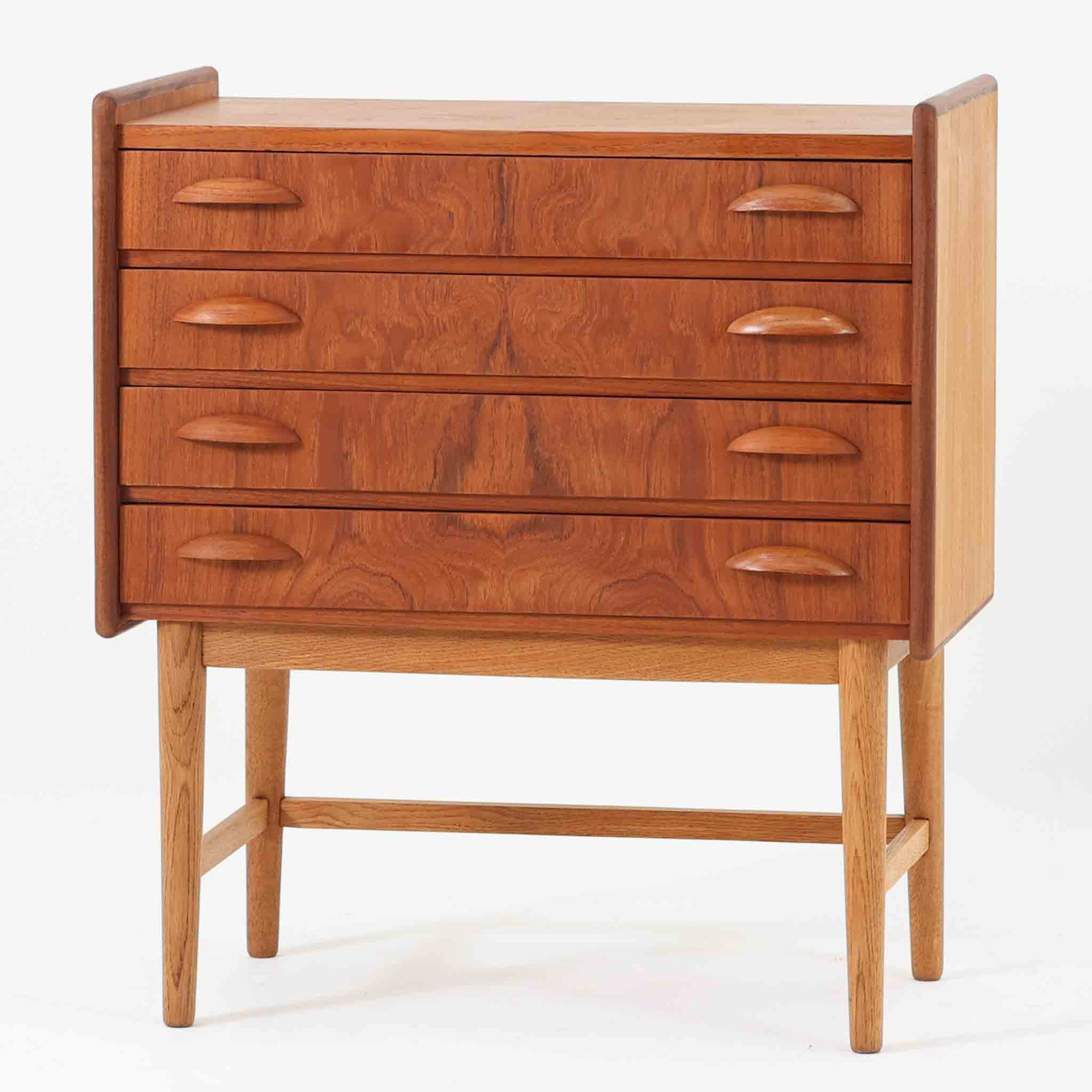 チーク材とオーク材を組み合わせた4段チェストです。前板には美しい木目を持つチーク材、脚部には明るく堅牢なオーク材が用いられ、素材のコントラストが北欧らしい洗練された印象を与えます。緩やかな曲線を描く取手や、すっきりとしたプロポーションが全体を端正にまとめ、コンパクトな幅59cmながら十分な収納力を備えています。リビングや寝室、書斎などさまざまな空間に取り入れやすく、ビンテージならではの風合いと実用性を兼ね備えた一台です。