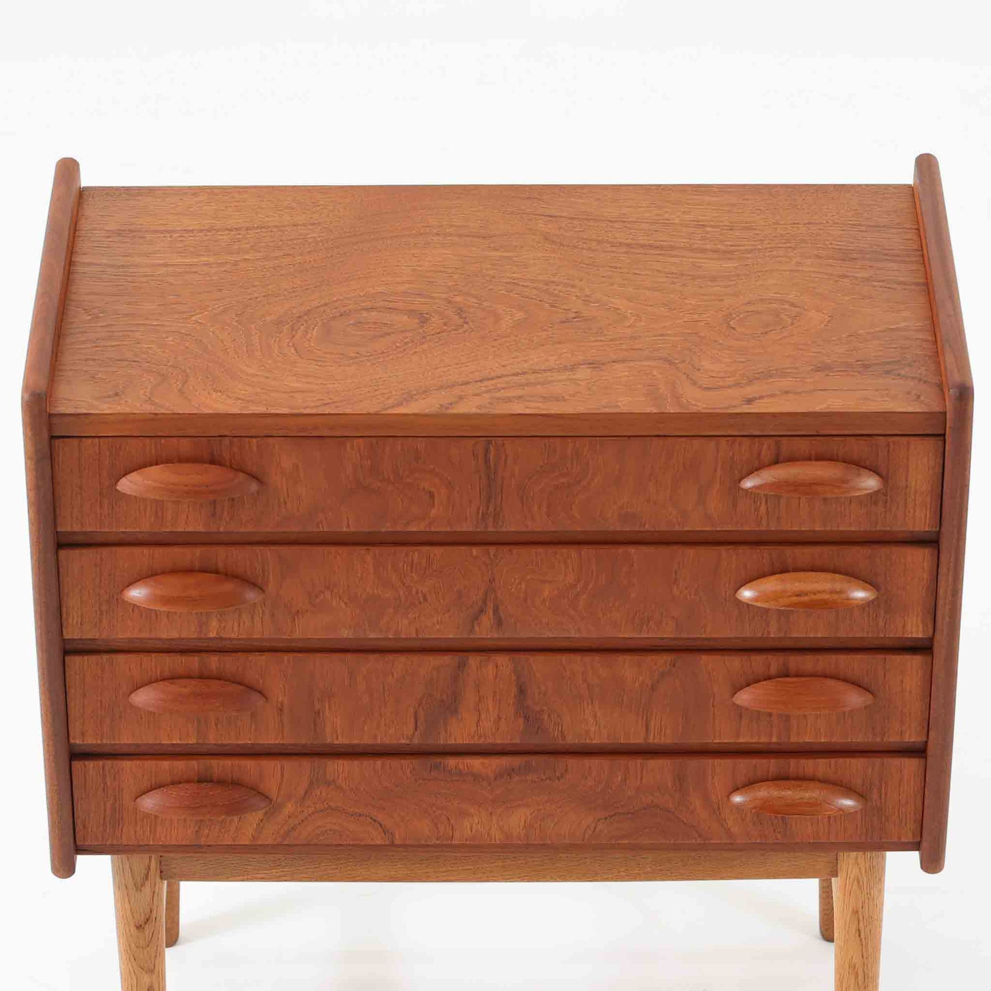 チーク材とオーク材を組み合わせた4段チェストです。前板には美しい木目を持つチーク材、脚部には明るく堅牢なオーク材が用いられ、素材のコントラストが北欧らしい洗練された印象を与えます。緩やかな曲線を描く取手や、すっきりとしたプロポーションが全体を端正にまとめ、コンパクトな幅59cmながら十分な収納力を備えています。リビングや寝室、書斎などさまざまな空間に取り入れやすく、ビンテージならではの風合いと実用性を兼ね備えた一台です。