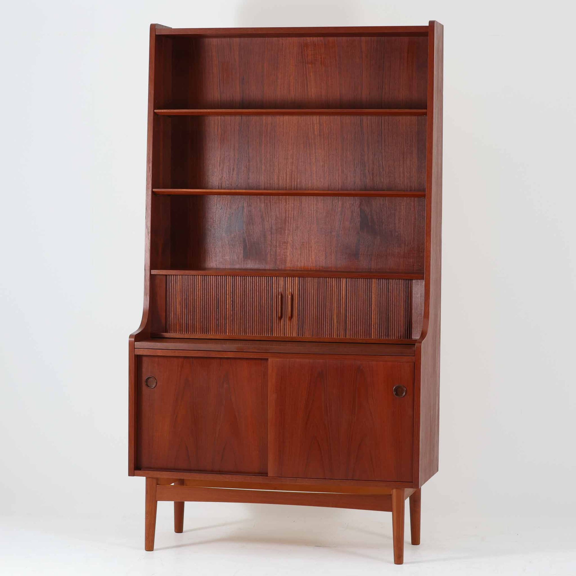 Johannes Sorthがデザインし、Nexo Mobelfabrikが製作したディスプレイシェルフです。美しいチーク材の深みある木目を活かした端正なフォルムに、蛇腹扉を備えた収納部が上質なアクセントとなっています。上部のオープン棚はお気に入りの器や書籍、オブジェを美しく飾ることができ、中段の細かな仕切りや小引き出しは書類や小物整理にも便利。下部の引き戸収納まで備えた実用性の高い構成で、リビングや書斎で見せる収納と隠す収納を両立します。経年で深みを増した木肌と職人技が、北欧ビンテージならではの存在感を放つ希少な一台です。