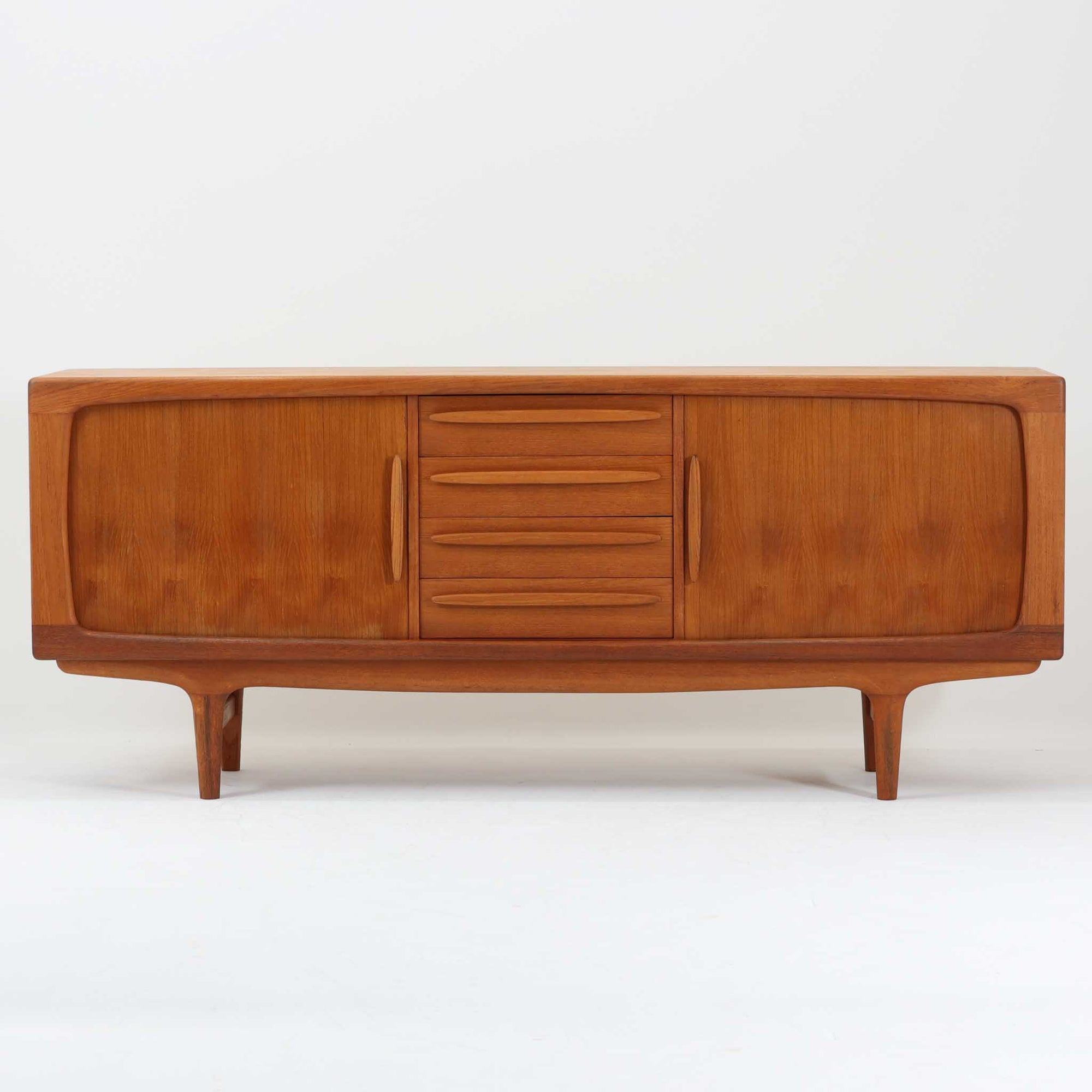 Johannes Andersenがデザインし、C.F.C. Silkeborgが製作した幅200cmのサイドボードです。チーク材の豊かな木目を活かした滑らかな曲面フレームと、横へ流れるように開閉する蛇腹扉が印象的で、端正さの中に軽やかなリズムを生み出します。中央の4段引き出しと両側の収納スペースにより高い収納力を備え、内部の棚板は可動式で実用性も良好。すらりと伸びる脚部が全体に洗練された印象を与え、空間に北欧ビンテージならではの気品と存在感をもたらします。