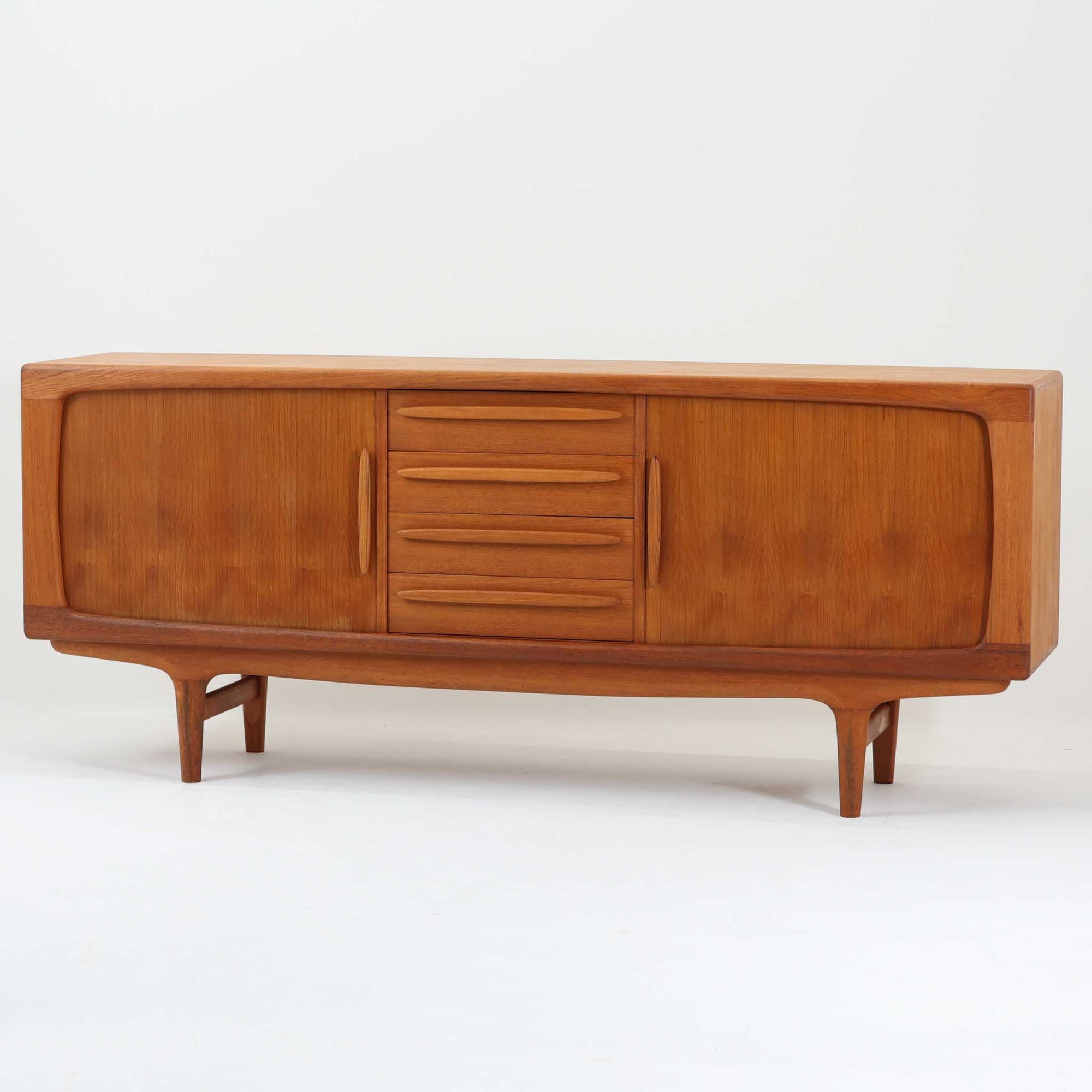 Johannes Andersenがデザインし、C.F.C. Silkeborgが製作した幅200cmのサイドボードです。チーク材の豊かな木目を活かした滑らかな曲面フレームと、横へ流れるように開閉する蛇腹扉が印象的で、端正さの中に軽やかなリズムを生み出します。中央の4段引き出しと両側の収納スペースにより高い収納力を備え、内部の棚板は可動式で実用性も良好。すらりと伸びる脚部が全体に洗練された印象を与え、空間に北欧ビンテージならではの気品と存在感をもたらします。