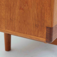 Johannes Andersenがデザインし、C.F.C. Silkeborgが製作した幅200cmのサイドボードです。チーク材の豊かな木目を活かした滑らかな曲面フレームと、横へ流れるように開閉する蛇腹扉が印象的で、端正さの中に軽やかなリズムを生み出します。中央の4段引き出しと両側の収納スペースにより高い収納力を備え、内部の棚板は可動式で実用性も良好。すらりと伸びる脚部が全体に洗練された印象を与え、空間に北欧ビンテージならではの気品と存在感をもたらします。