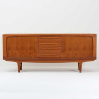 Johannes Andersenがデザインし、C.F.C. Silkeborgが製作した幅200cmのサイドボードです。チーク材の豊かな木目を活かした滑らかな曲面フレームと、横へ流れるように開閉する蛇腹扉が印象的で、端正さの中に軽やかなリズムを生み出します。中央の4段引き出しと両側の収納スペースにより高い収納力を備え、内部の棚板は可動式で実用性も良好。すらりと伸びる脚部が全体に洗練された印象を与え、空間に北欧ビンテージならではの気品と存在感をもたらします。