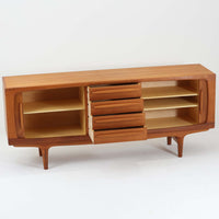 Johannes Andersenがデザインし、C.F.C. Silkeborgが製作した幅200cmのサイドボードです。チーク材の豊かな木目を活かした滑らかな曲面フレームと、横へ流れるように開閉する蛇腹扉が印象的で、端正さの中に軽やかなリズムを生み出します。中央の4段引き出しと両側の収納スペースにより高い収納力を備え、内部の棚板は可動式で実用性も良好。すらりと伸びる脚部が全体に洗練された印象を与え、空間に北欧ビンテージならではの気品と存在感をもたらします。