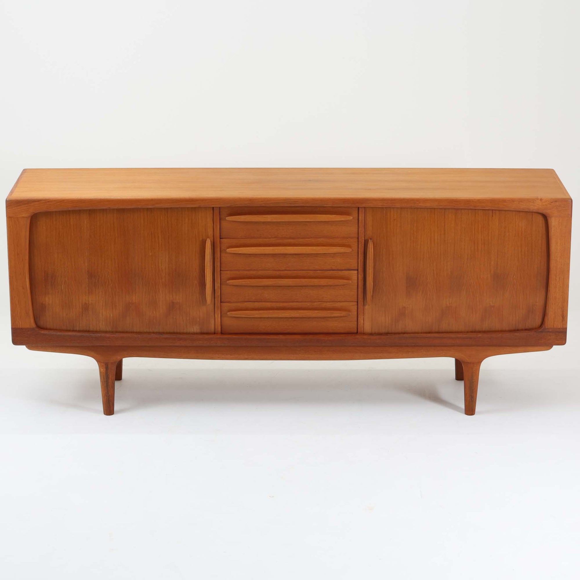 Johannes Andersenがデザインし、C.F.C. Silkeborgが製作した幅200cmのサイドボードです。チーク材の豊かな木目を活かした滑らかな曲面フレームと、横へ流れるように開閉する蛇腹扉が印象的で、端正さの中に軽やかなリズムを生み出します。中央の4段引き出しと両側の収納スペースにより高い収納力を備え、内部の棚板は可動式で実用性も良好。すらりと伸びる脚部が全体に洗練された印象を与え、空間に北欧ビンテージならではの気品と存在感をもたらします。