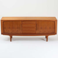 Johannes Andersenがデザインし、C.F.C. Silkeborgが製作した幅200cmのサイドボードです。チーク材の豊かな木目を活かした滑らかな曲面フレームと、横へ流れるように開閉する蛇腹扉が印象的で、端正さの中に軽やかなリズムを生み出します。中央の4段引き出しと両側の収納スペースにより高い収納力を備え、内部の棚板は可動式で実用性も良好。すらりと伸びる脚部が全体に洗練された印象を与え、空間に北欧ビンテージならではの気品と存在感をもたらします。