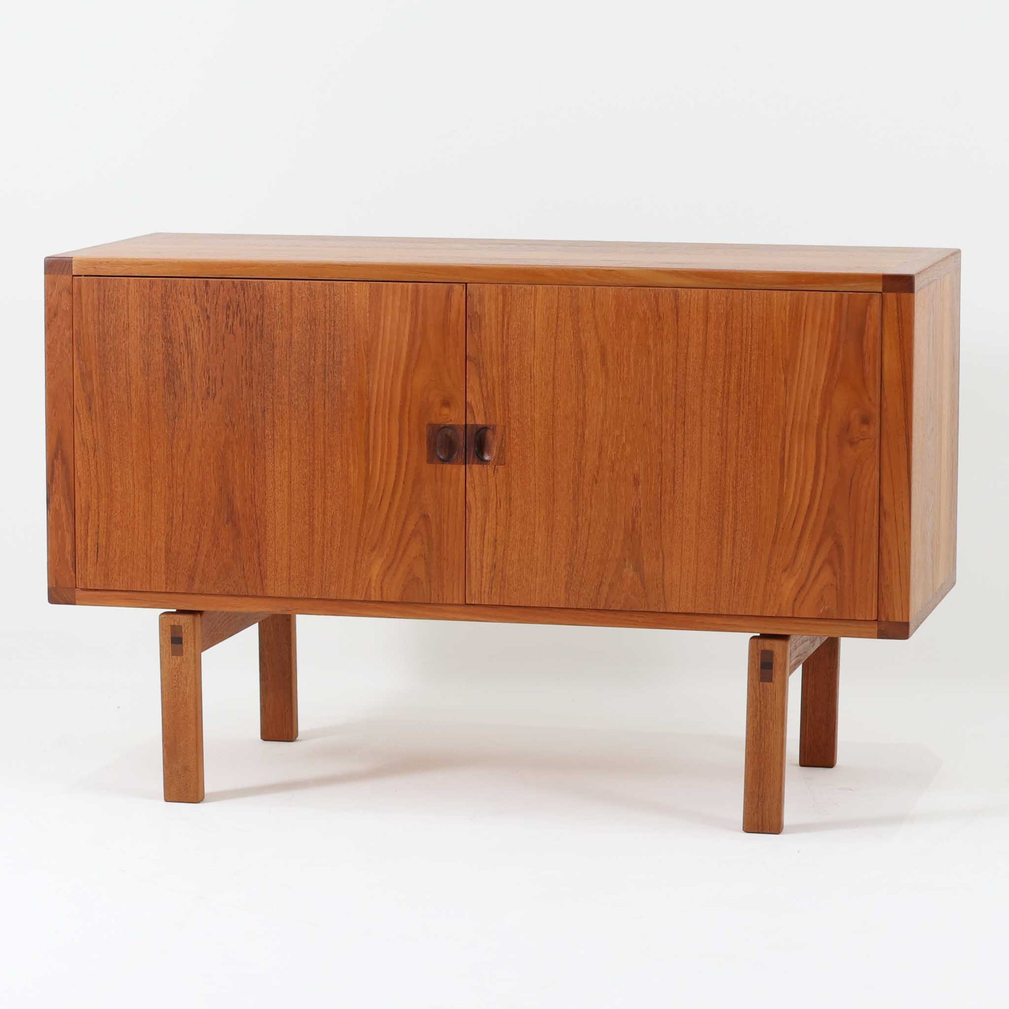 レナート・ベンダーがデザインし、Ulferts Mobler社により製作されたCoronaキャビネットは、小ぶりなサイズ感と端正な佇まいが魅力の北欧ビンテージ家具です。チーク材の美しい木目を活かしたシンプルな箱型構造に、脚部の控えめな意匠が軽やかさを添えています。取っ手部分には異素材となるローズウッドが用いられており、チーク材とのコントラストがさりげないアクセントとして全体の表情を引き締めています。内部は使いやすい収納空間を備え、食器や書類、小物類の整理に適しており、リビングや書斎、玄関周りなど幅広いシーンで活躍します。年月を経て深みを増した素材感と、丁寧な作りが感じられる一台です。