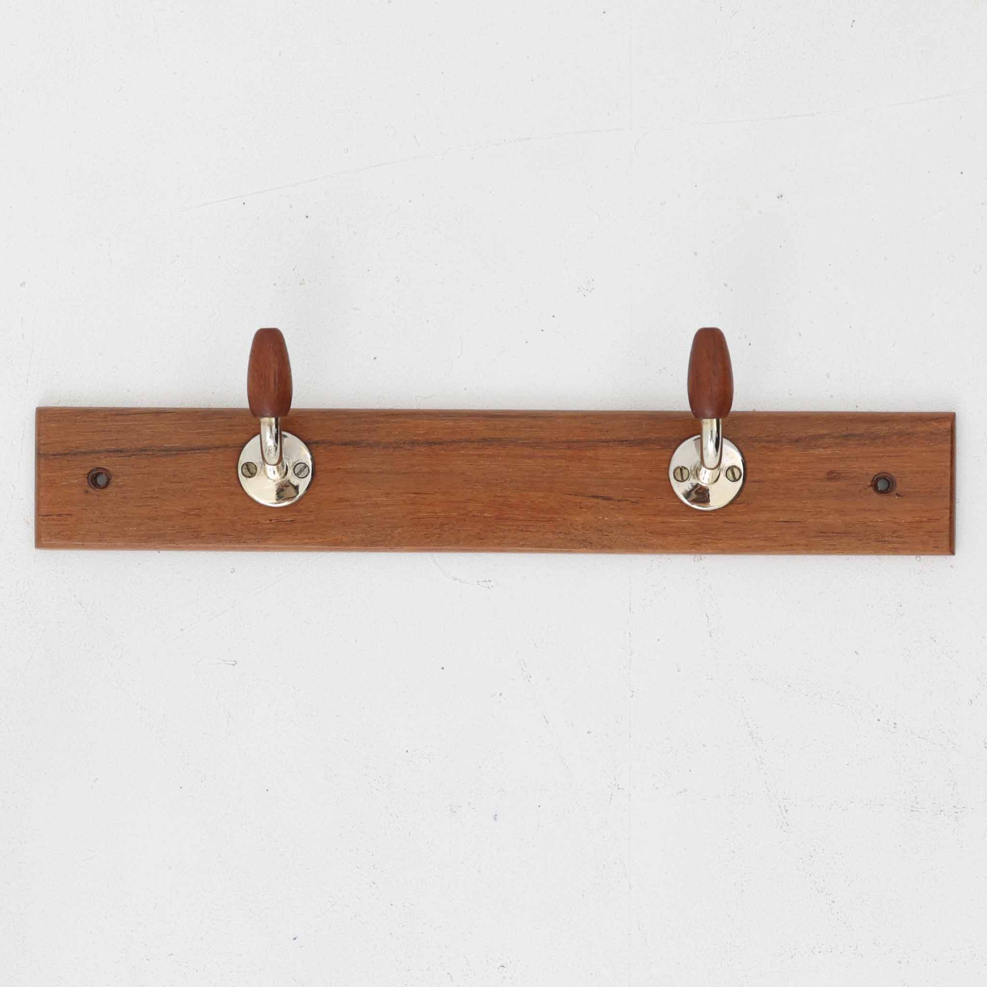 チーク材のベースにメタルフックを組み合わせたデンマーク製の2連ウォールハンガーで、先端には丸みのある木製キャップが付いており掛けた衣類やバッグに優しく、シンプルながら北欧ビンテージらしい温かみのある素材感が魅力です。玄関や寝室、キッチン、ワークスペースなど壁面収納として幅広く活躍し、単体使いはもちろん複数並べて設置することで統一感のあるディスプレイも楽しめます。コンパクトで設置しやすく暮らしの中で気軽に取り入れやすいアイテムです。