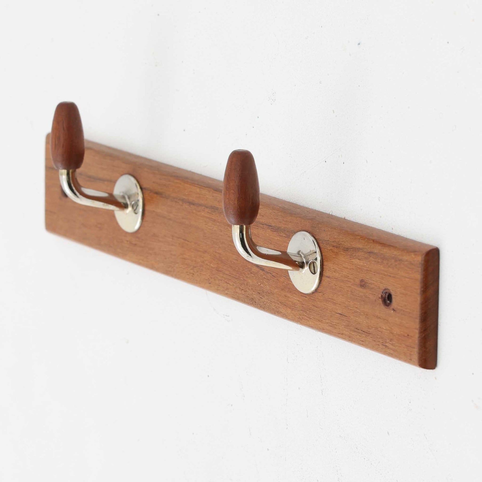 チーク材のベースにメタルフックを組み合わせたデンマーク製の2連ウォールハンガーで、先端には丸みのある木製キャップが付いており掛けた衣類やバッグに優しく、シンプルながら北欧ビンテージらしい温かみのある素材感が魅力です。玄関や寝室、キッチン、ワークスペースなど壁面収納として幅広く活躍し、単体使いはもちろん複数並べて設置することで統一感のあるディスプレイも楽しめます。コンパクトで設置しやすく暮らしの中で気軽に取り入れやすいアイテムです。