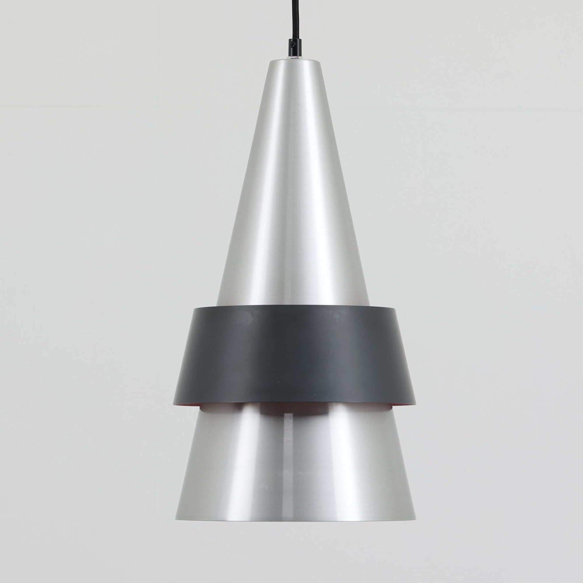 Jo HammerborgがFog & Morupのために手掛けた「Corona」は、直径22cmとコンパクトながら全高45cmと縦にしっかりとした存在感を持つアルミ×スチール製ペンダントライトで、上下に伸びる円錐形フォルムと中央のブラックバンドが彫刻的な印象を与える北欧ビンテージ品です。光源を囲む二重構造によって眩しさを抑えつつ下方向へ明かりを集中的に落とす設計となっており、ダイニングやカウンター上での1灯使用はもちろん、複数灯を並べても空間にリズムを生み出します。経年で深まった素材の風合いがハーマボーらしいモダンな佇まいを際立たせ、空間のアクセントとしても十分な存在感を発揮します。