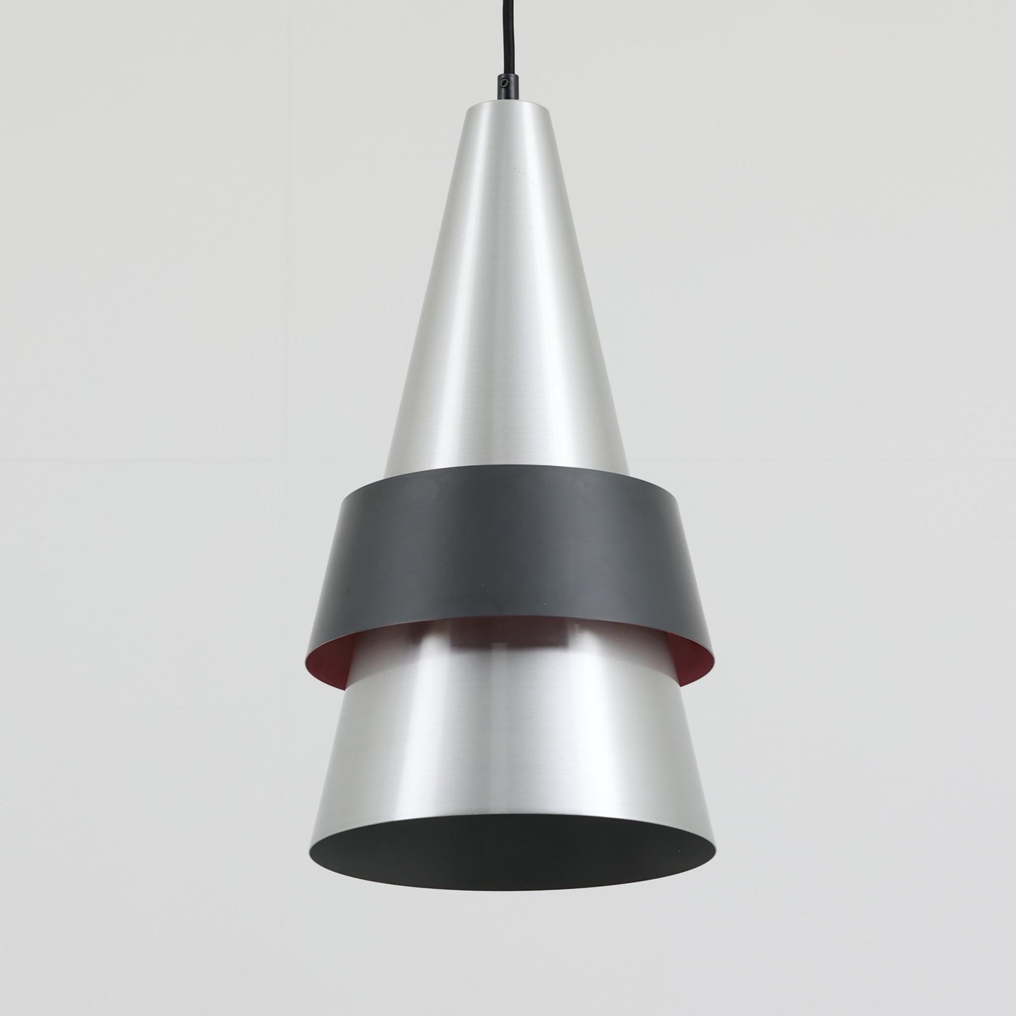 Jo HammerborgがFog &amp; Morupのために手掛けた「Corona」は、直径22cmとコンパクトながら全高45cmと縦にしっかりとした存在感を持つアルミ×スチール製ペンダントライトで、上下に伸びる円錐形フォルムと中央のブラックバンドが彫刻的な印象を与える北欧ビンテージ品です。光源を囲む二重構造によって眩しさを抑えつつ下方向へ明かりを集中的に落とす設計となっており、ダイニングやカウンター上での1灯使用はもちろん、複数灯を並べても空間にリズムを生み出します。経年で深まった素材の風合いがハーマボーらしいモダンな佇まいを際立たせ、空間のアクセントとしても十分な存在感を発揮します。