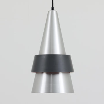 Jo HammerborgがFog & Morupのために手掛けた「Corona」は、直径22cmとコンパクトながら全高45cmと縦にしっかりとした存在感を持つアルミ×スチール製ペンダントライトで、上下に伸びる円錐形フォルムと中央のブラックバンドが彫刻的な印象を与える北欧ビンテージ品です。光源を囲む二重構造によって眩しさを抑えつつ下方向へ明かりを集中的に落とす設計となっており、ダイニングやカウンター上での1灯使用はもちろん、複数灯を並べても空間にリズムを生み出します。経年で深まった素材の風合いがハーマボーらしいモダンな佇まいを際立たせ、空間のアクセントとしても十分な存在感を発揮します。