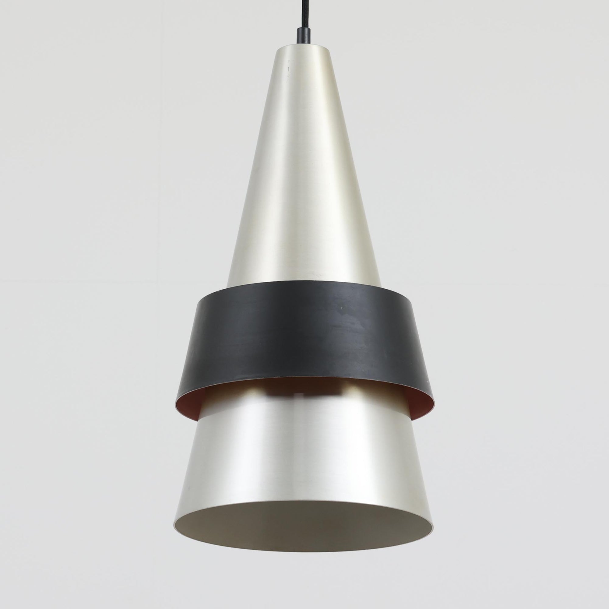 Jo HammerborgがFog &amp; Morupのために手掛けた「Corona」は、直径22cmとコンパクトながら全高45cmと縦にしっかりとした存在感を持つアルミ×スチール製ペンダントライトで、上下に伸びる円錐形フォルムと中央のブラックバンドが彫刻的な印象を与える北欧ビンテージ品です。光源を囲む二重構造によって眩しさを抑えつつ下方向へ明かりを集中的に落とす設計となっており、ダイニングやカウンター上での1灯使用はもちろん、複数灯を並べても空間にリズムを生み出します。経年で深まった素材の風合いがハーマボーらしいモダンな佇まいを際立たせ、空間のアクセントとしても十分な存在感を発揮します。