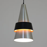 Jo HammerborgがFog & Morupのために手掛けた「Corona」は、直径22cmとコンパクトながら全高45cmと縦にしっかりとした存在感を持つアルミ×スチール製ペンダントライトで、上下に伸びる円錐形フォルムと中央のブラックバンドが彫刻的な印象を与える北欧ビンテージ品です。光源を囲む二重構造によって眩しさを抑えつつ下方向へ明かりを集中的に落とす設計となっており、ダイニングやカウンター上での1灯使用はもちろん、複数灯を並べても空間にリズムを生み出します。経年で深まった素材の風合いがハーマボーらしいモダンな佇まいを際立たせ、空間のアクセントとしても十分な存在感を発揮します。