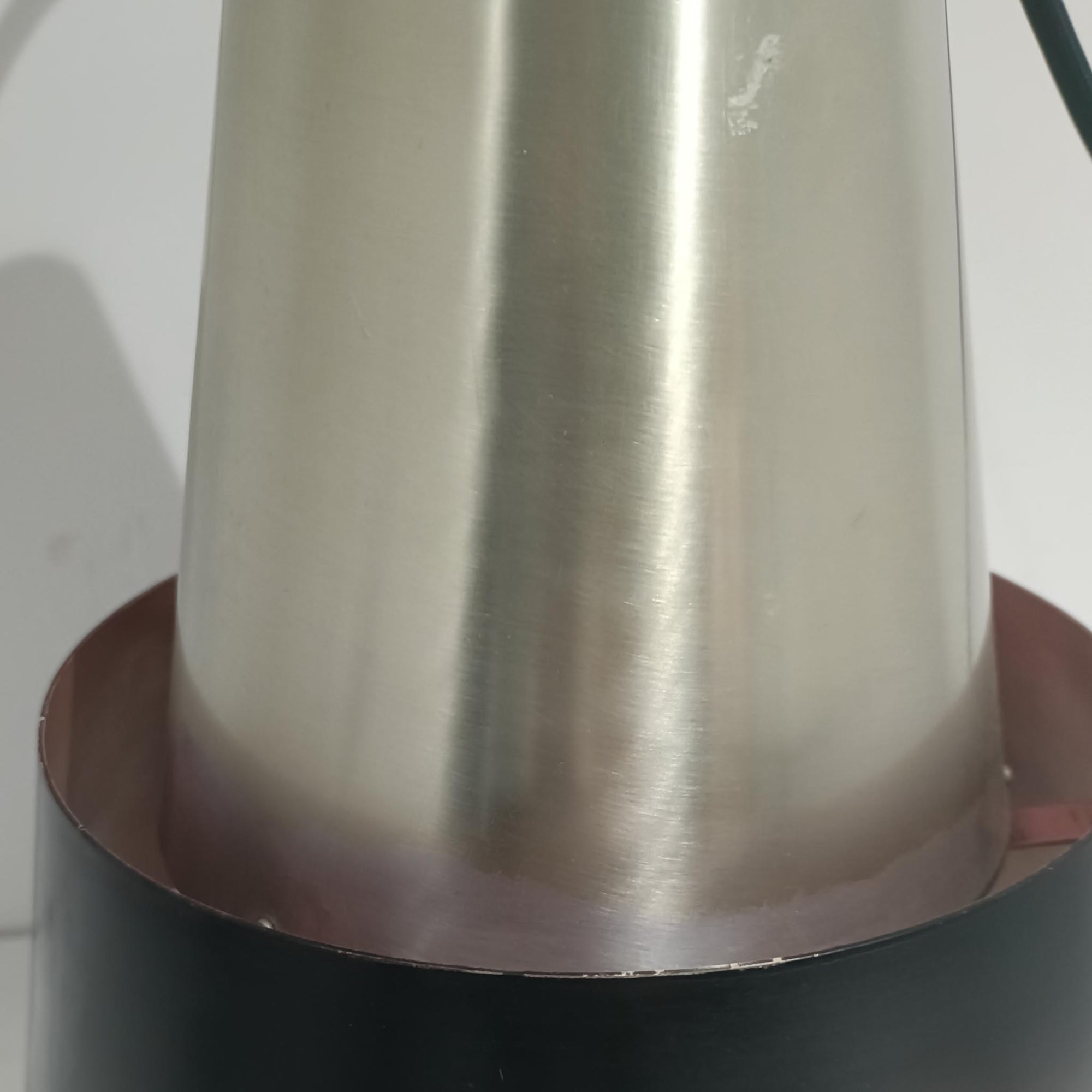 Jo HammerborgがFog &amp; Morupのために手掛けた「Corona」は、直径22cmとコンパクトながら全高45cmと縦にしっかりとした存在感を持つアルミ×スチール製ペンダントライトで、上下に伸びる円錐形フォルムと中央のブラックバンドが彫刻的な印象を与える北欧ビンテージ品です。光源を囲む二重構造によって眩しさを抑えつつ下方向へ明かりを集中的に落とす設計となっており、ダイニングやカウンター上での1灯使用はもちろん、複数灯を並べても空間にリズムを生み出します。経年で深まった素材の風合いがハーマボーらしいモダンな佇まいを際立たせ、空間のアクセントとしても十分な存在感を発揮します。