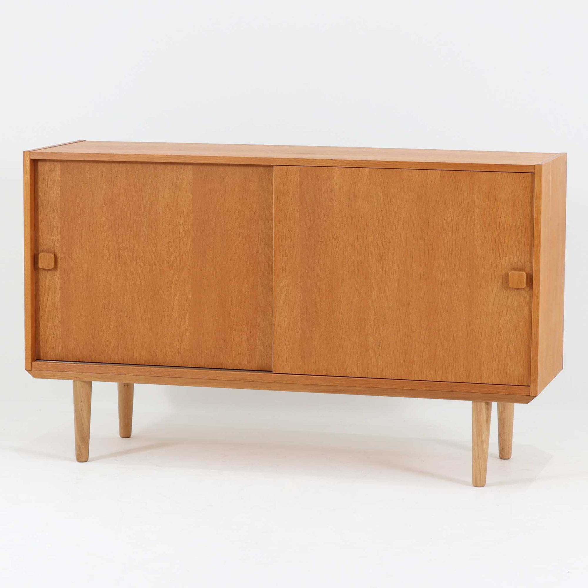 Domino Moblerが製作したデンマーク製ボードです。オーク材の明るく穏やかな木目を活かした端正なフレームです。引き戸構造により省スペースで使いやすく、内部には棚板を備え日用品や書類、食器などをすっきりと収納可能。幅122cmのバランスの取れたサイズ感で、リビングやダイニングのサイドキャビネットとしても活躍します。経年で味わいを増した木肌が空間に温もりと北欧ビンテージらしい趣を添える一品です。