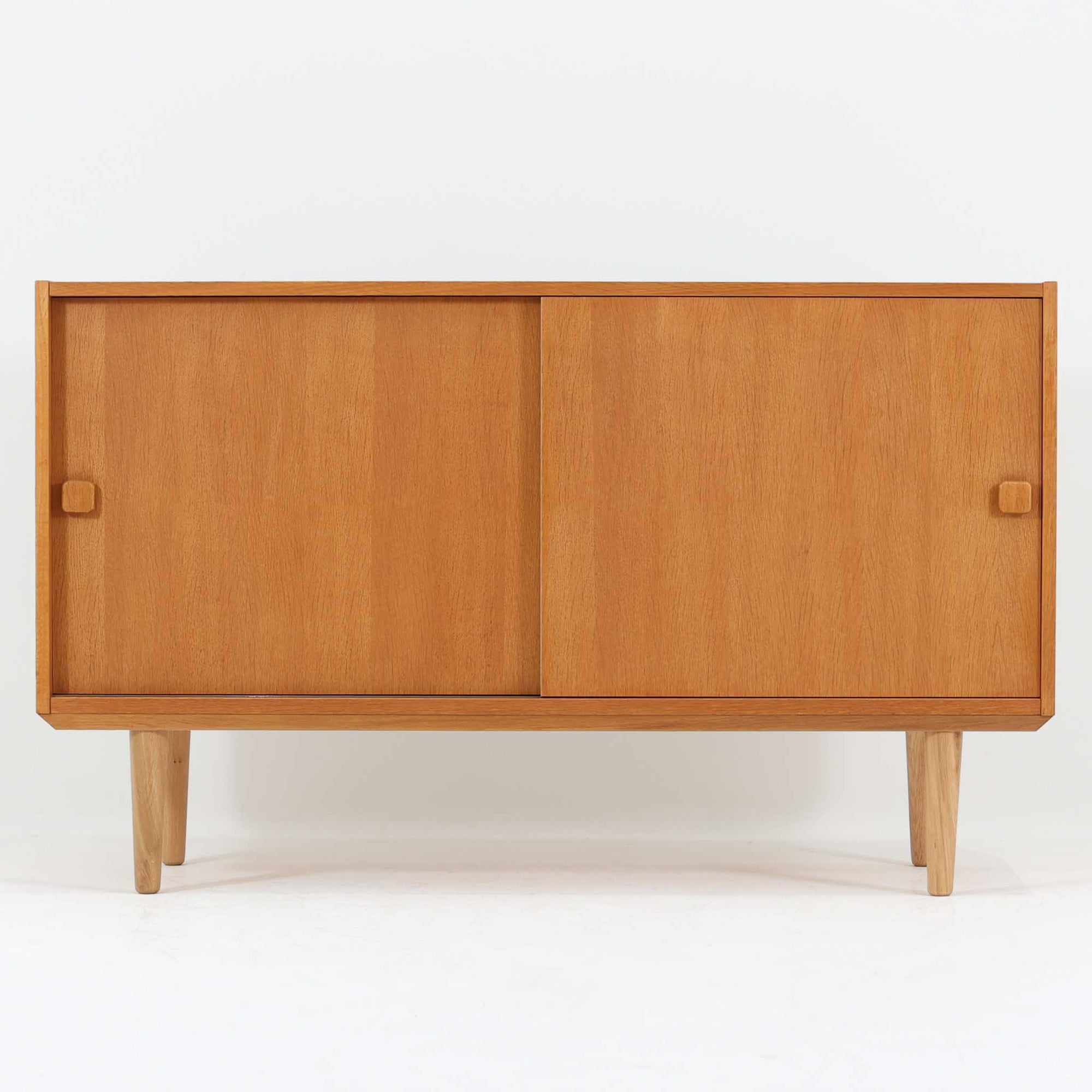 Domino Moblerが製作したデンマーク製ボードです。オーク材の明るく穏やかな木目を活かした端正なフレームです。引き戸構造により省スペースで使いやすく、内部には棚板を備え日用品や書類、食器などをすっきりと収納可能。幅122cmのバランスの取れたサイズ感で、リビングやダイニングのサイドキャビネットとしても活躍します。経年で味わいを増した木肌が空間に温もりと北欧ビンテージらしい趣を添える一品です。